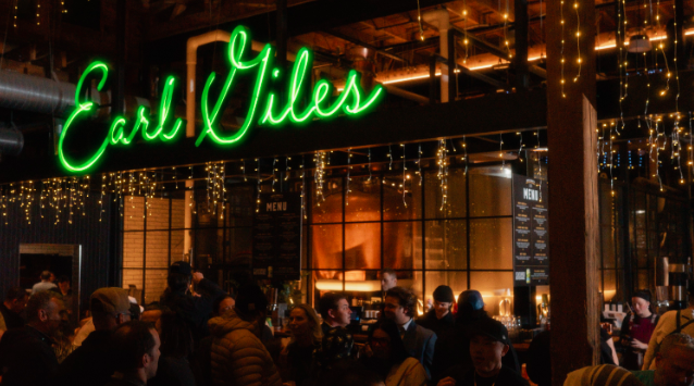 Crowded restaurant with a neon sign that reads 'Earl Giles' and string lights hanging inside.