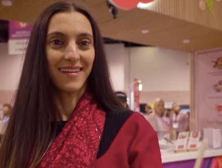 A woman with long dark hair smiling at an indoor event or exhibition.