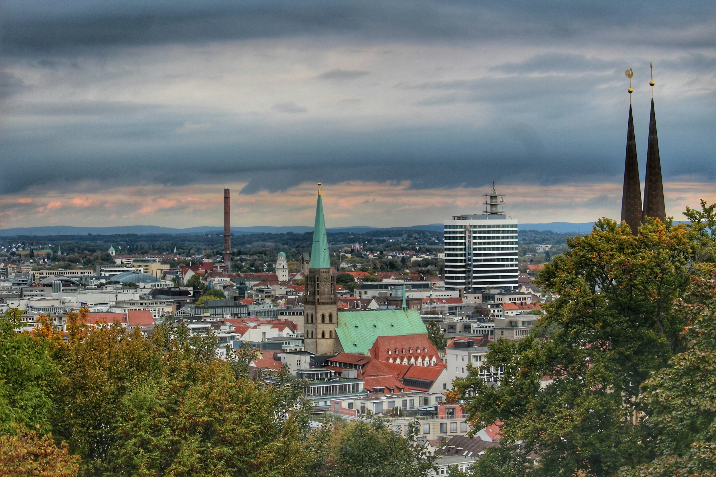 Stadtansicht mit Kirchen, modernen Gebäuden, Himmel, Bäumen im Vordergrund. Unser Stadt Bielefeld