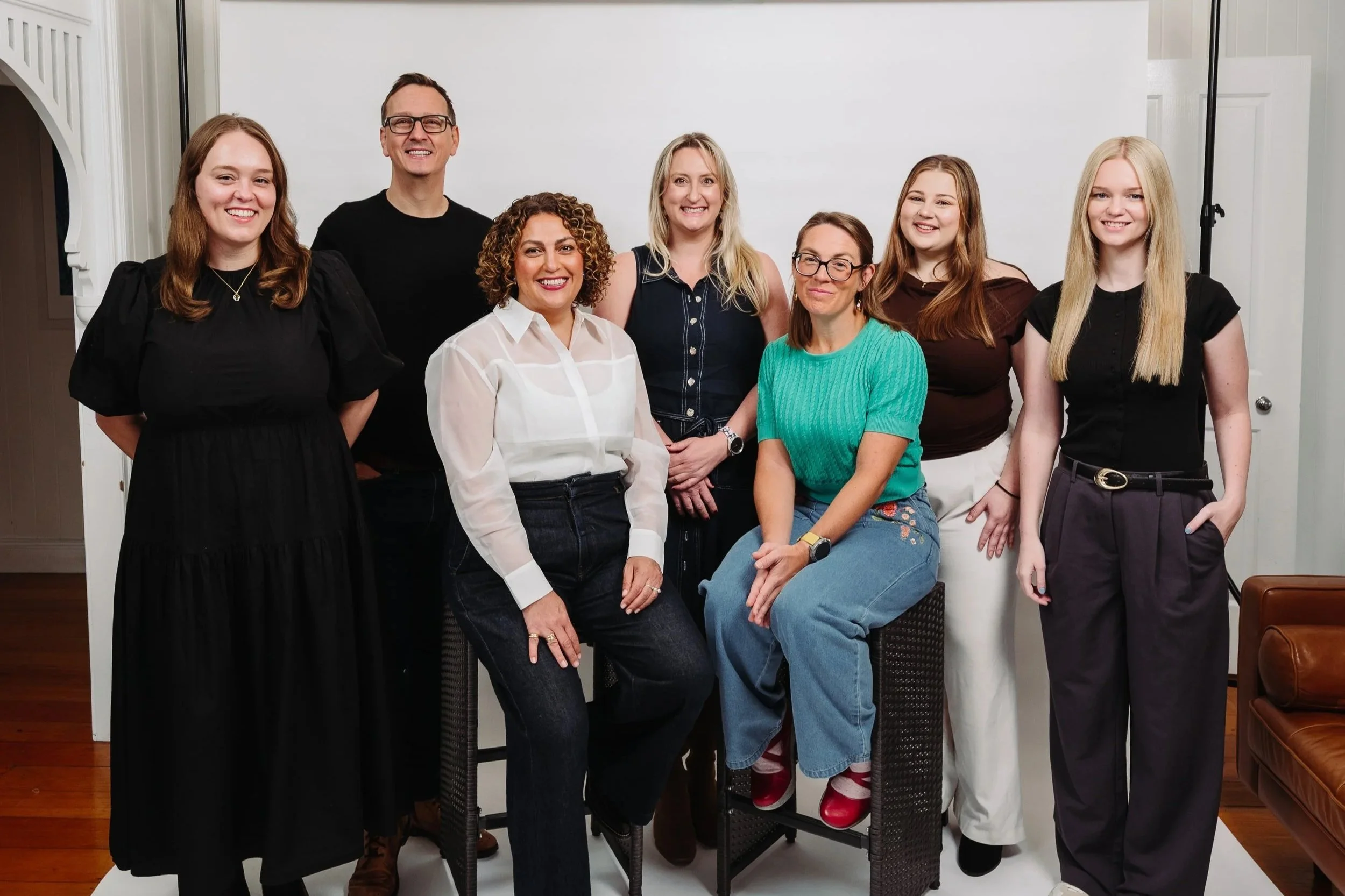 Group of nine diverse women and men smiling for a photo in an indoor studio with white background.