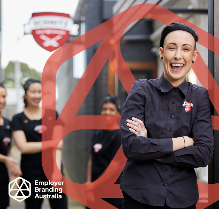 A group of four young women dressed in black uniform shirts, standing outside a building with a logo, smiling. The woman in the foreground, also in a black uniform shirt, is smiling and posed with arms crossed. There is a large red graphic overlay and a logo on the bottom left corner reading 'Employer Branding Australia'.
