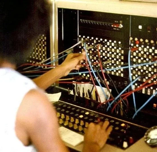 A person working with a vintage electronic or computer equipment, adjusting wires and knobs inside a large console or control panel.