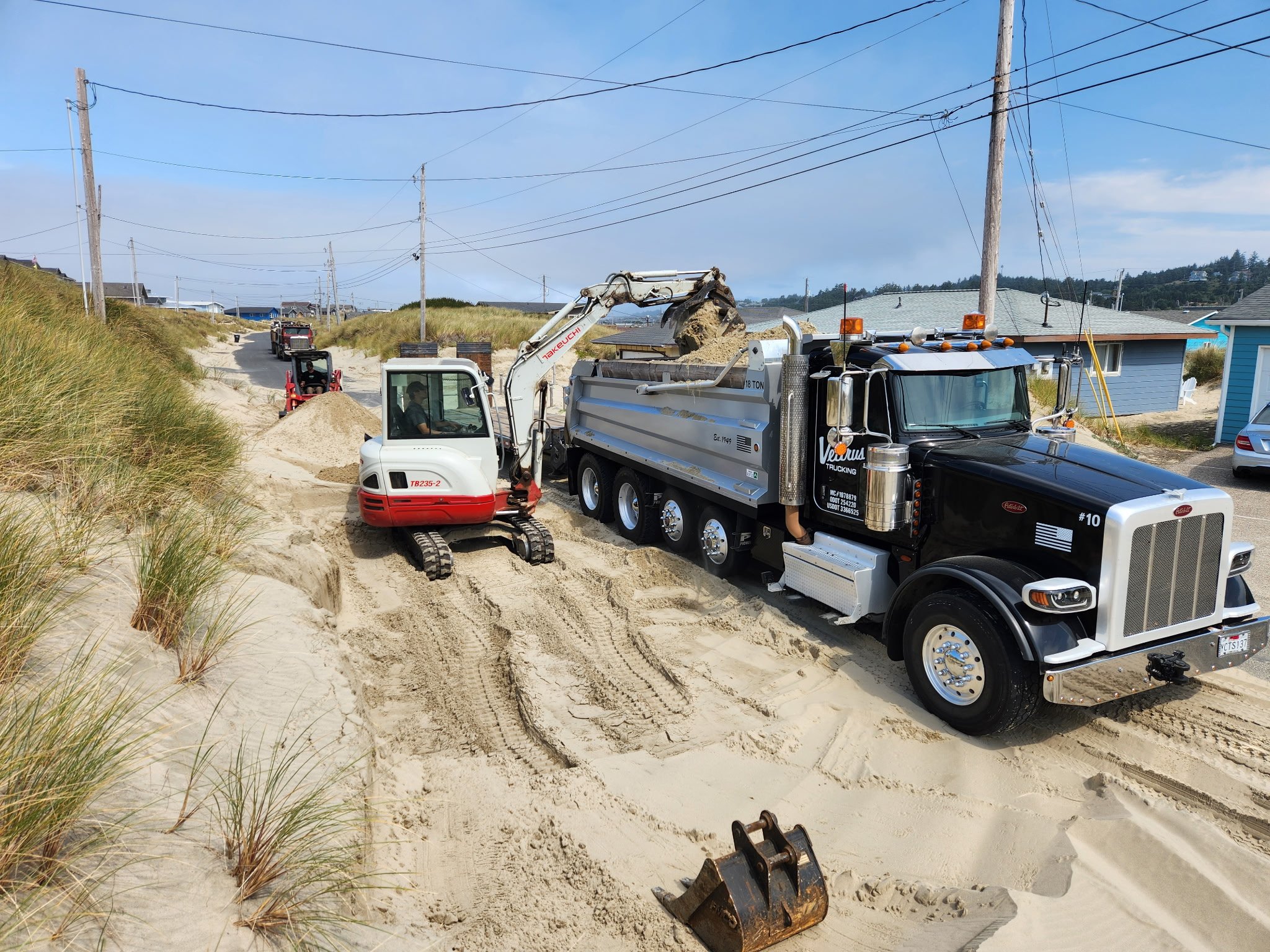 Construction equipment on sandy land near houses with power lines overhead. There are trucks, a small excavator, and building tools.
Bayshore Oregon sand removal