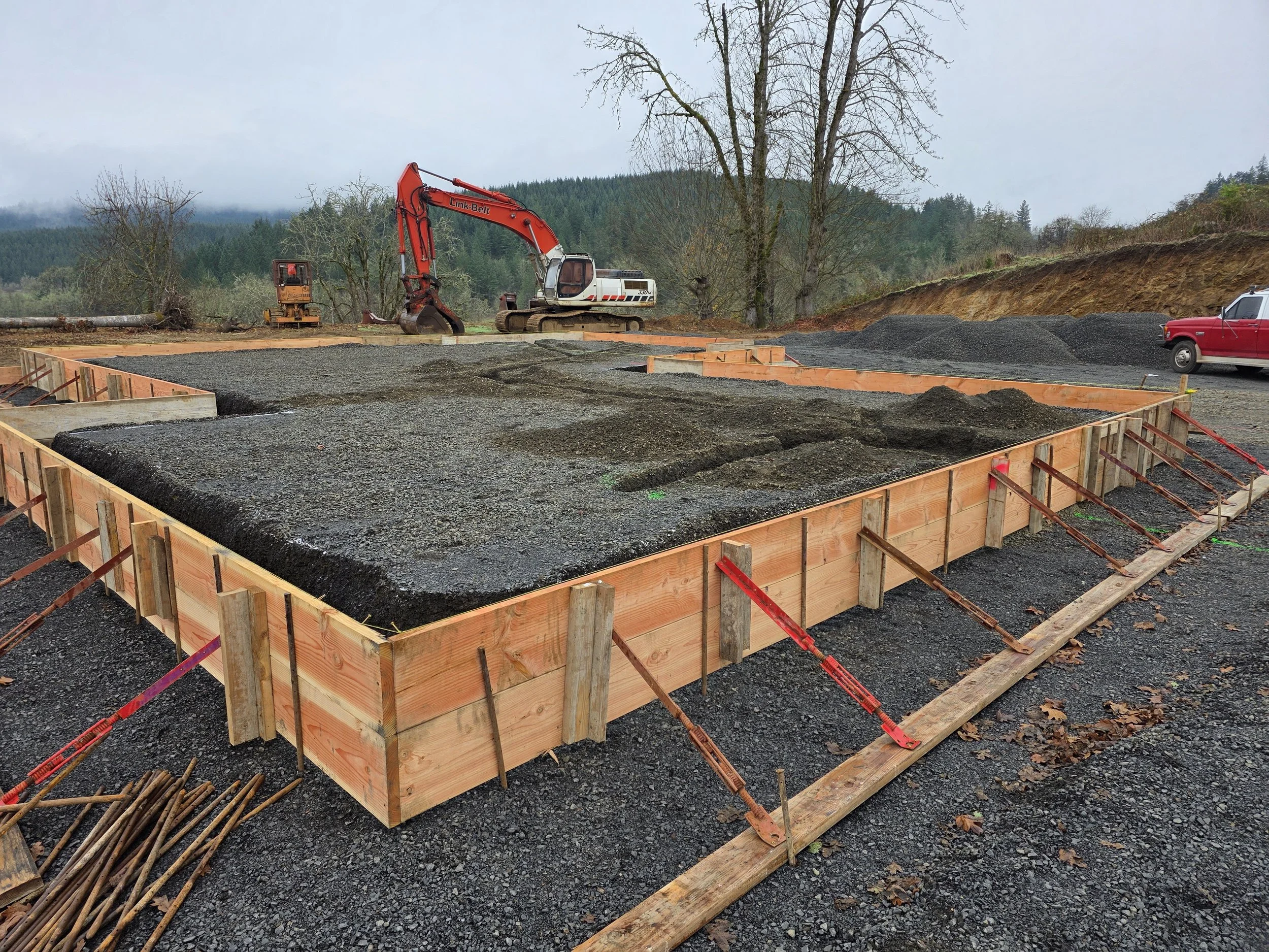 Construction site with a concrete foundation and wooden framing, Jackson's excavator in the back working in Salem Oregon.
