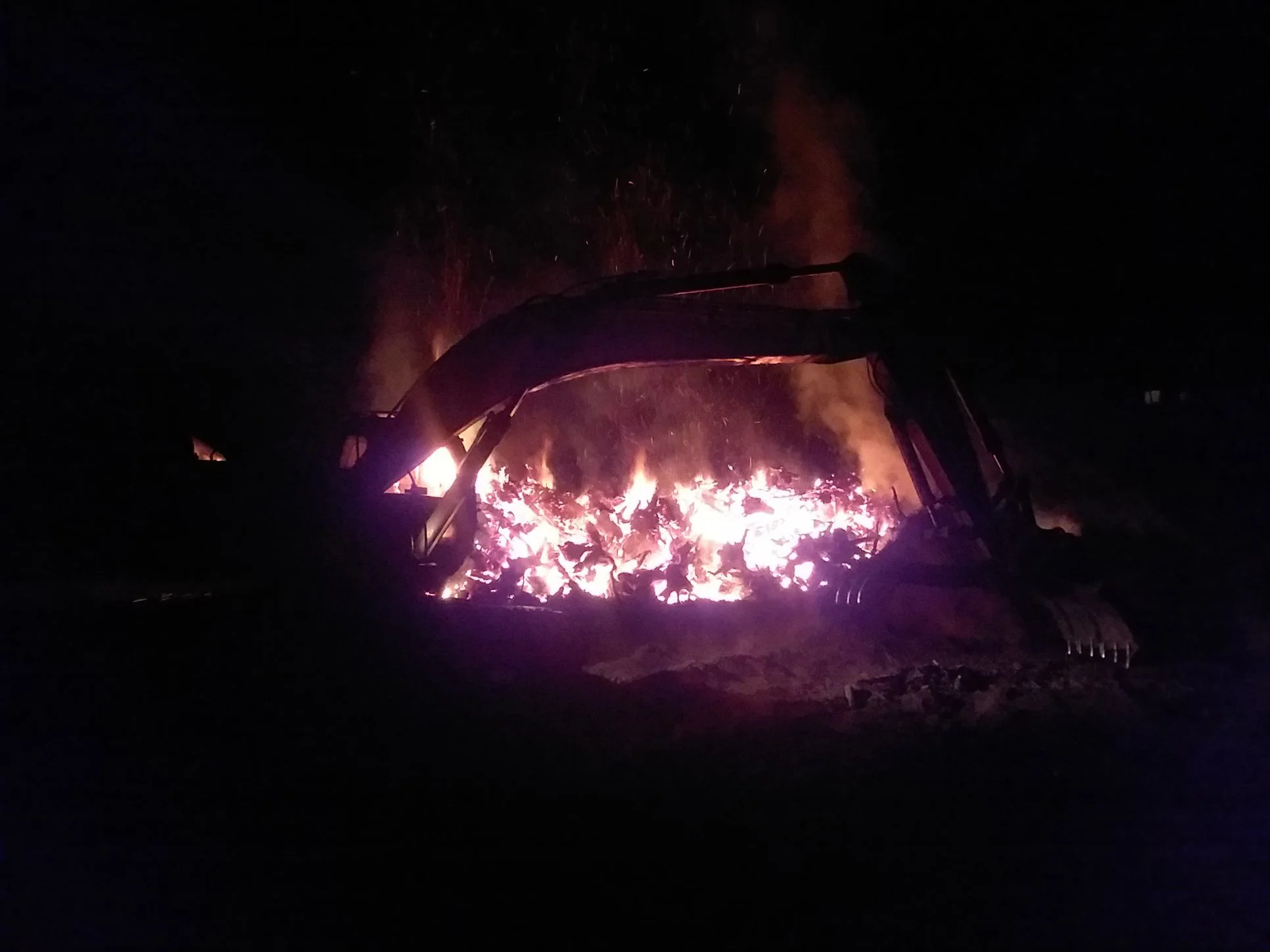 Nighttime scene of a campfire with glowing embers and sparks flying into the dark sky.