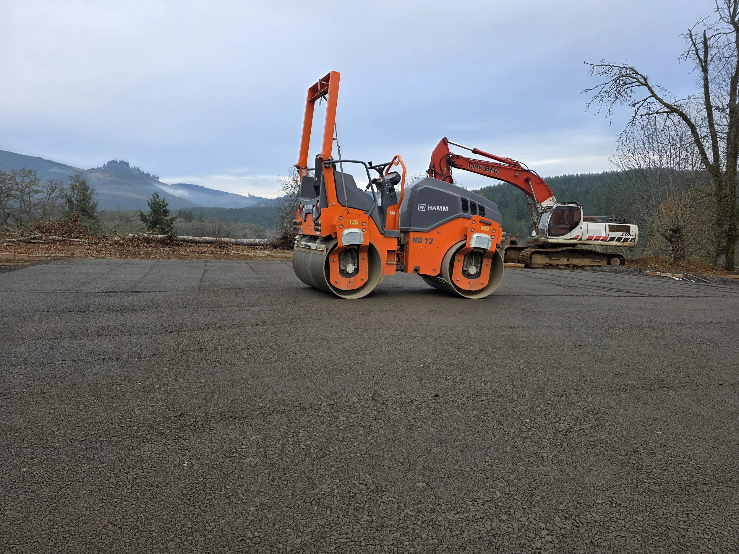 Construction equipment on a paved road with a mountainous landscape in the background. Brownsville Oregon. Compacting a house pad.