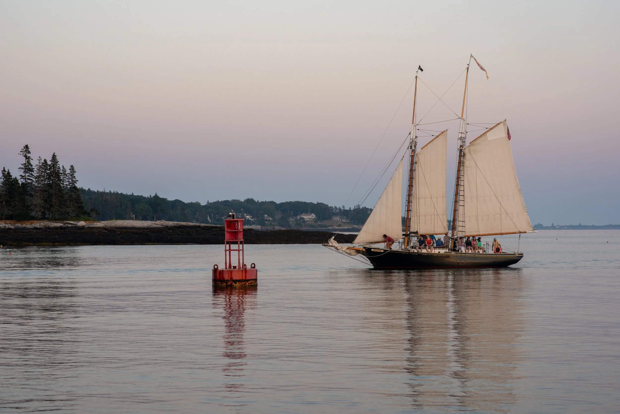 A sailboat glides across the water at sunset in Boothbay Harbor, Maine.