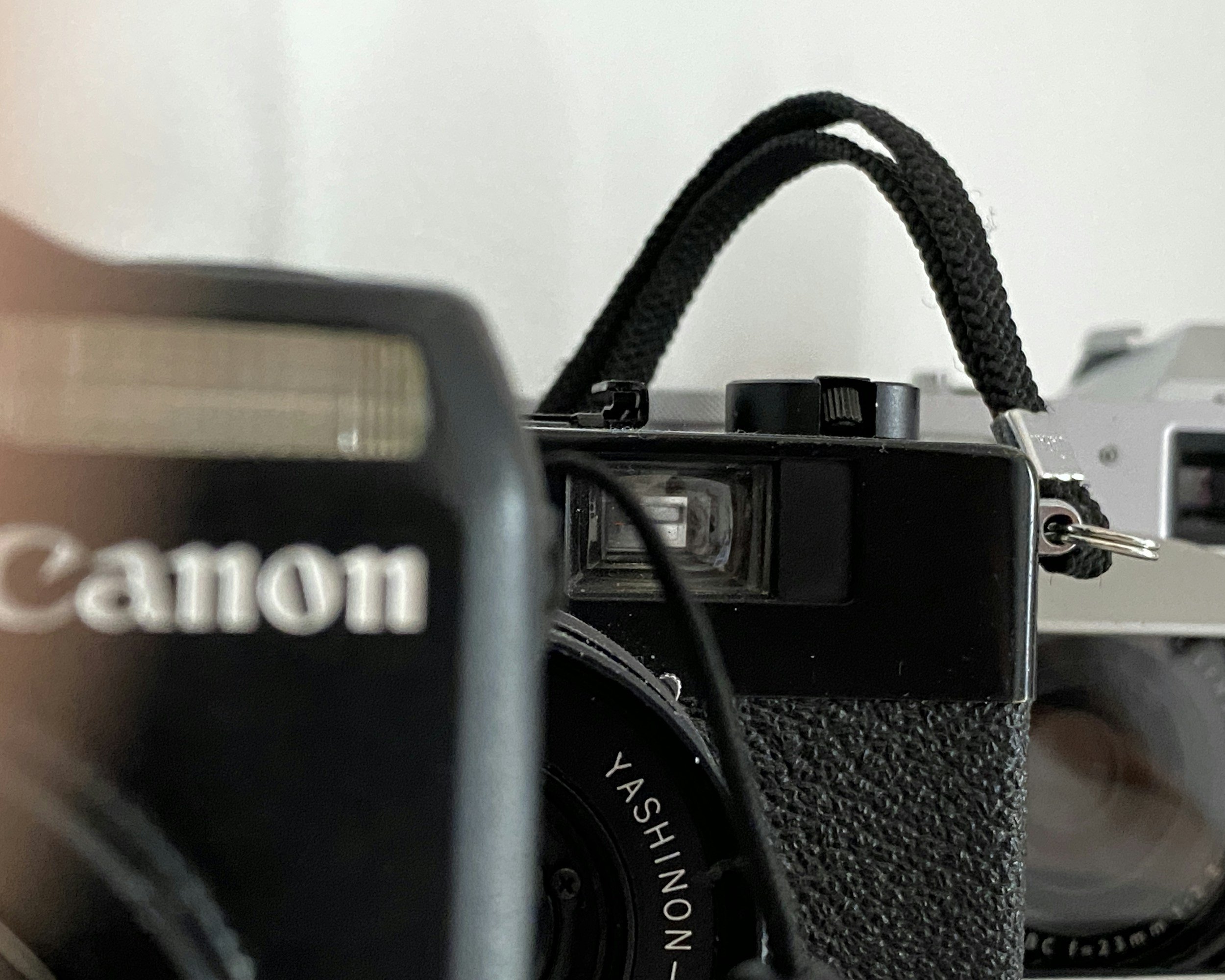 Close-up of two vintage cameras, one in black with a strap and the other in silver, with the lens and brand names partially visible.
