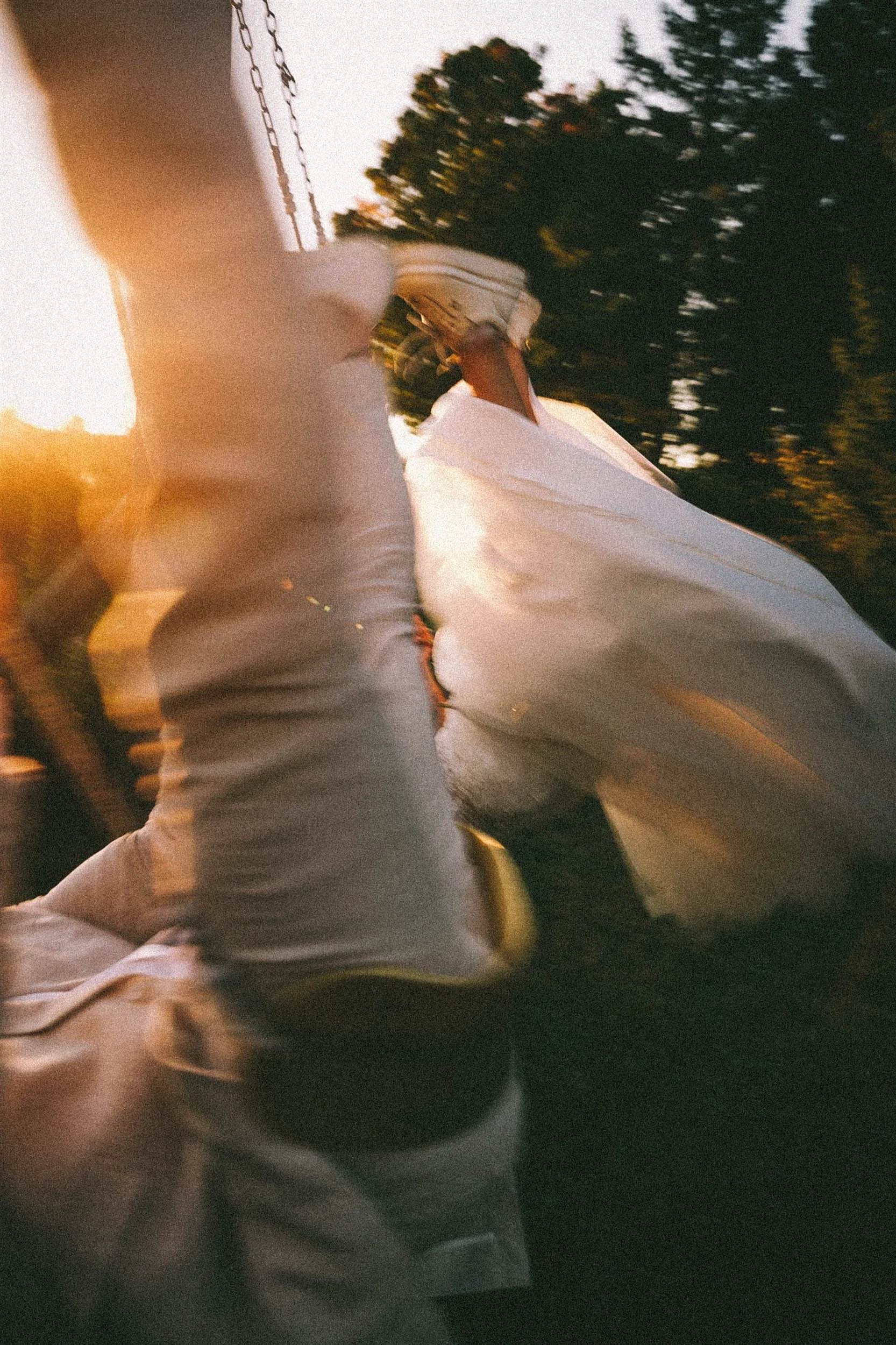 Person on a swing with white adidas sneakers and white pants, sunset in the background.