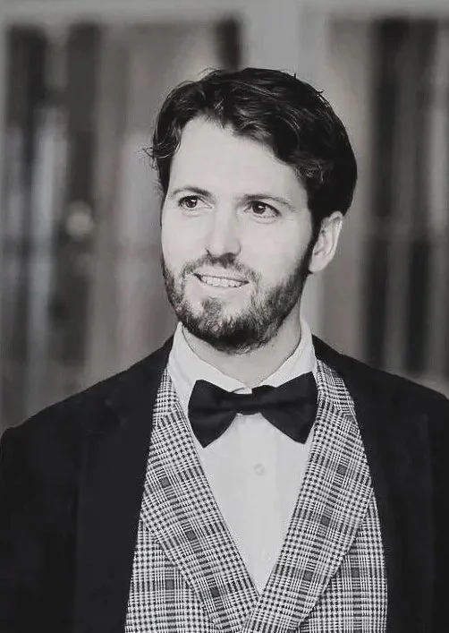 Black-and-white portrait of a smiling bearded man wearing a bow tie and patterned tuxedo jacket