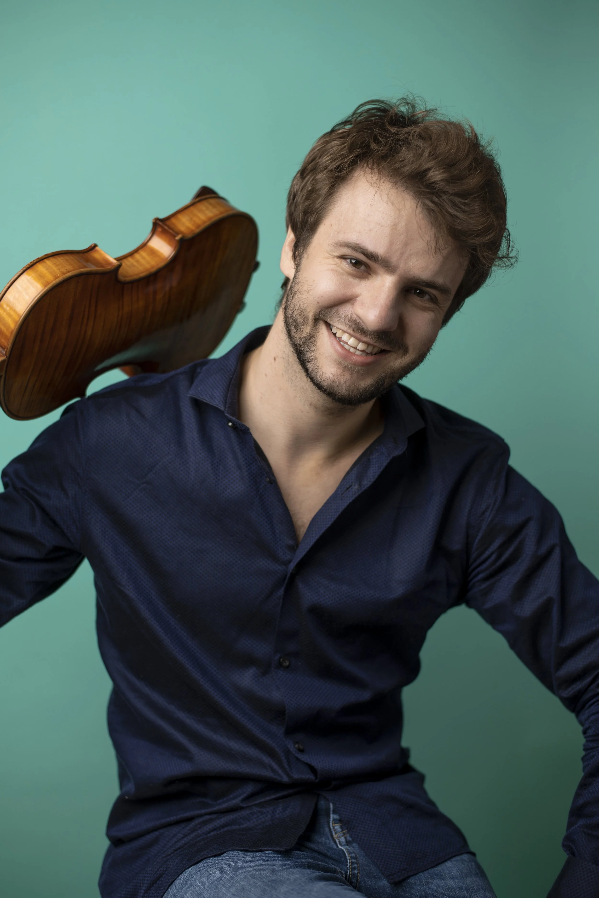 Smiling man in a navy shirt holding a violin against a teal background
