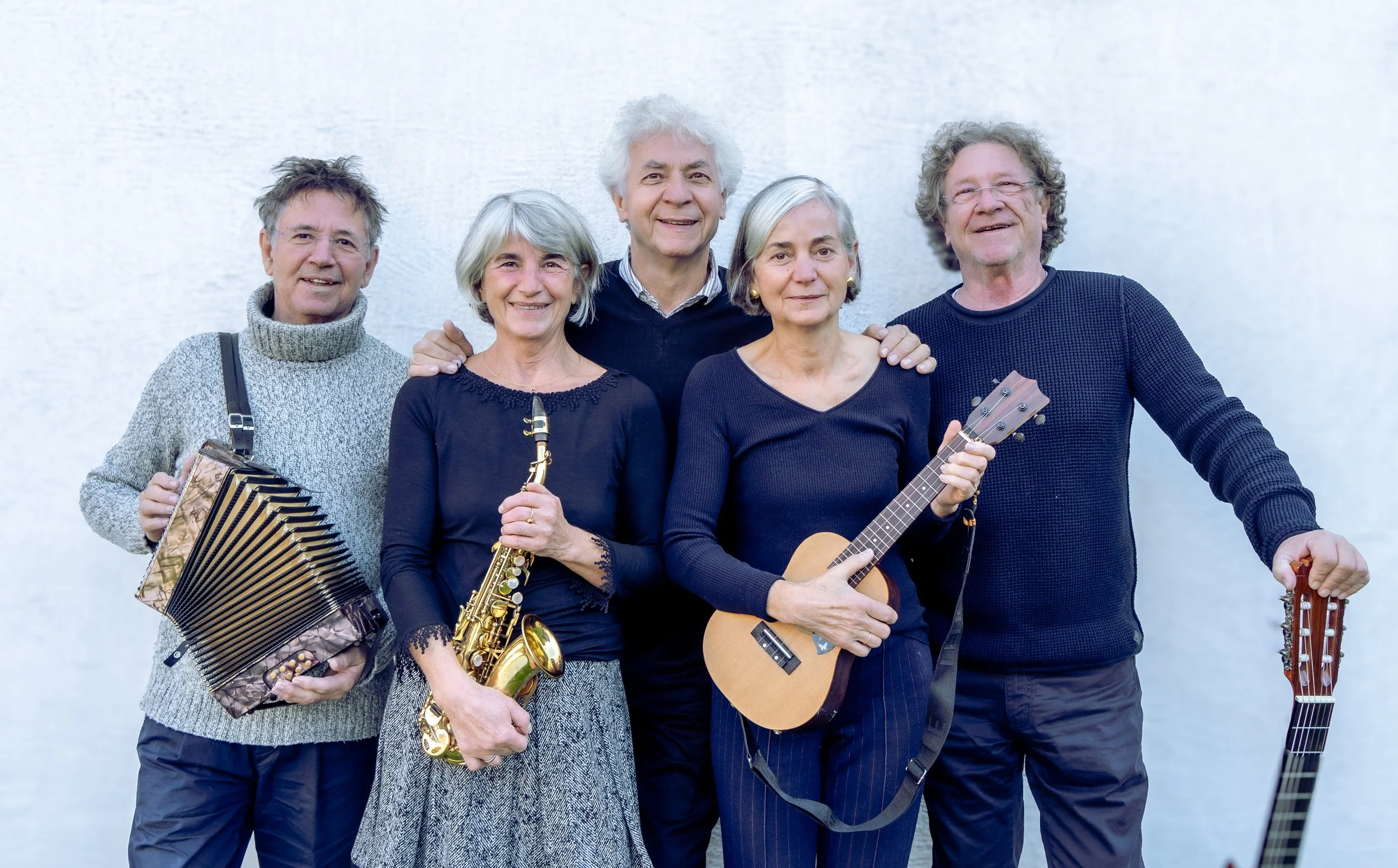 Five older musicians posing with an accordion, saxophone, ukulele, and guitar.