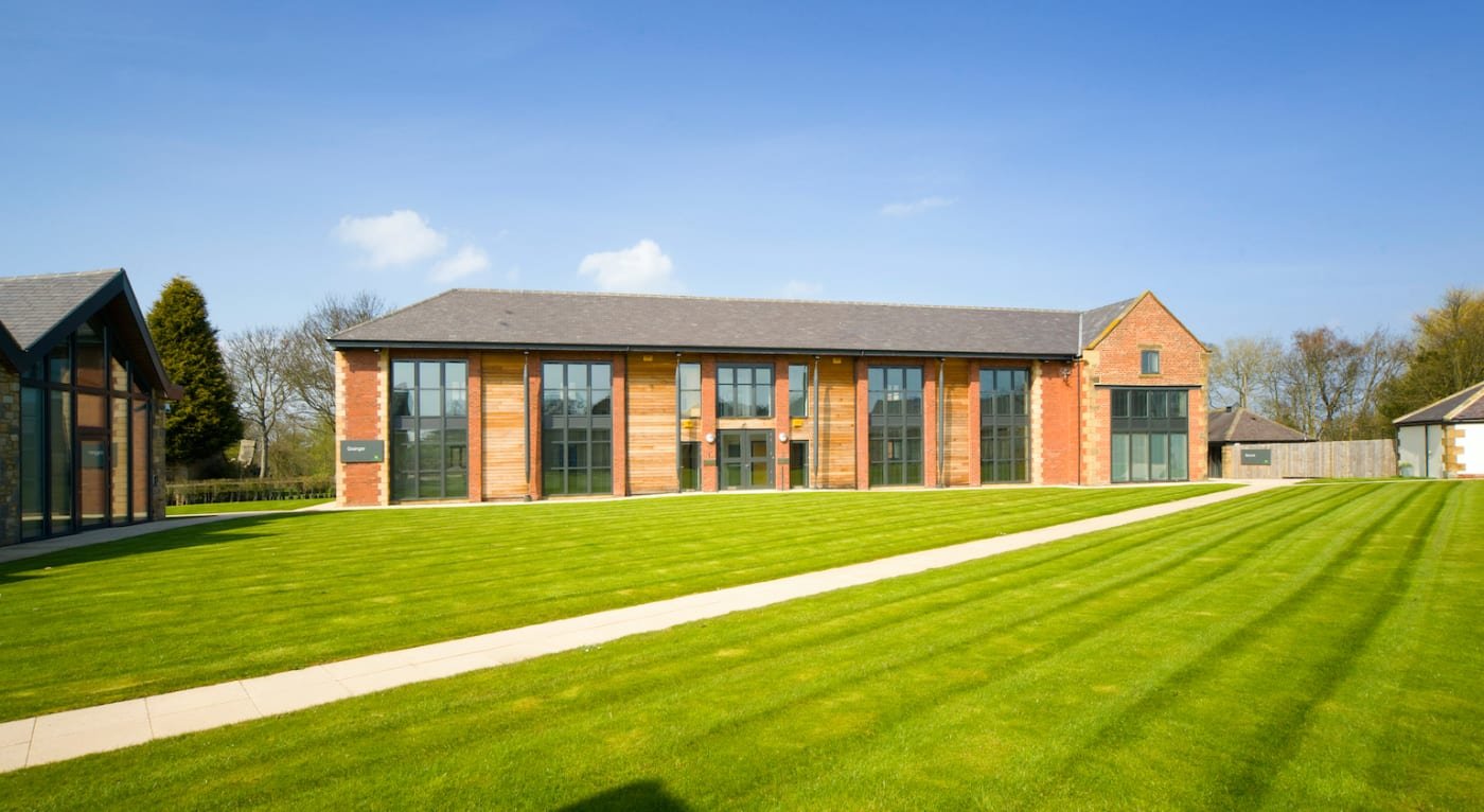 Modern office building at Prestwick Park with large glass windows, brick and wood exterior, surrounded by a well-maintained lawn and a clear blue sky.