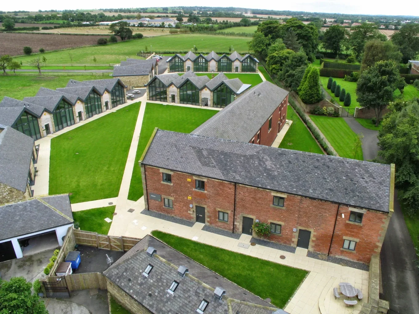 Aerial view of Prestwick Park modern office complex featuring large glass windows, surrounded by green lawns and trees, in a rural area with open fields in the background.