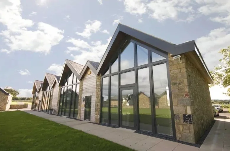Modern office building at Prestwick Park with large glass windows, stone walls, and a sloped roof, set against a partly cloudy sky.