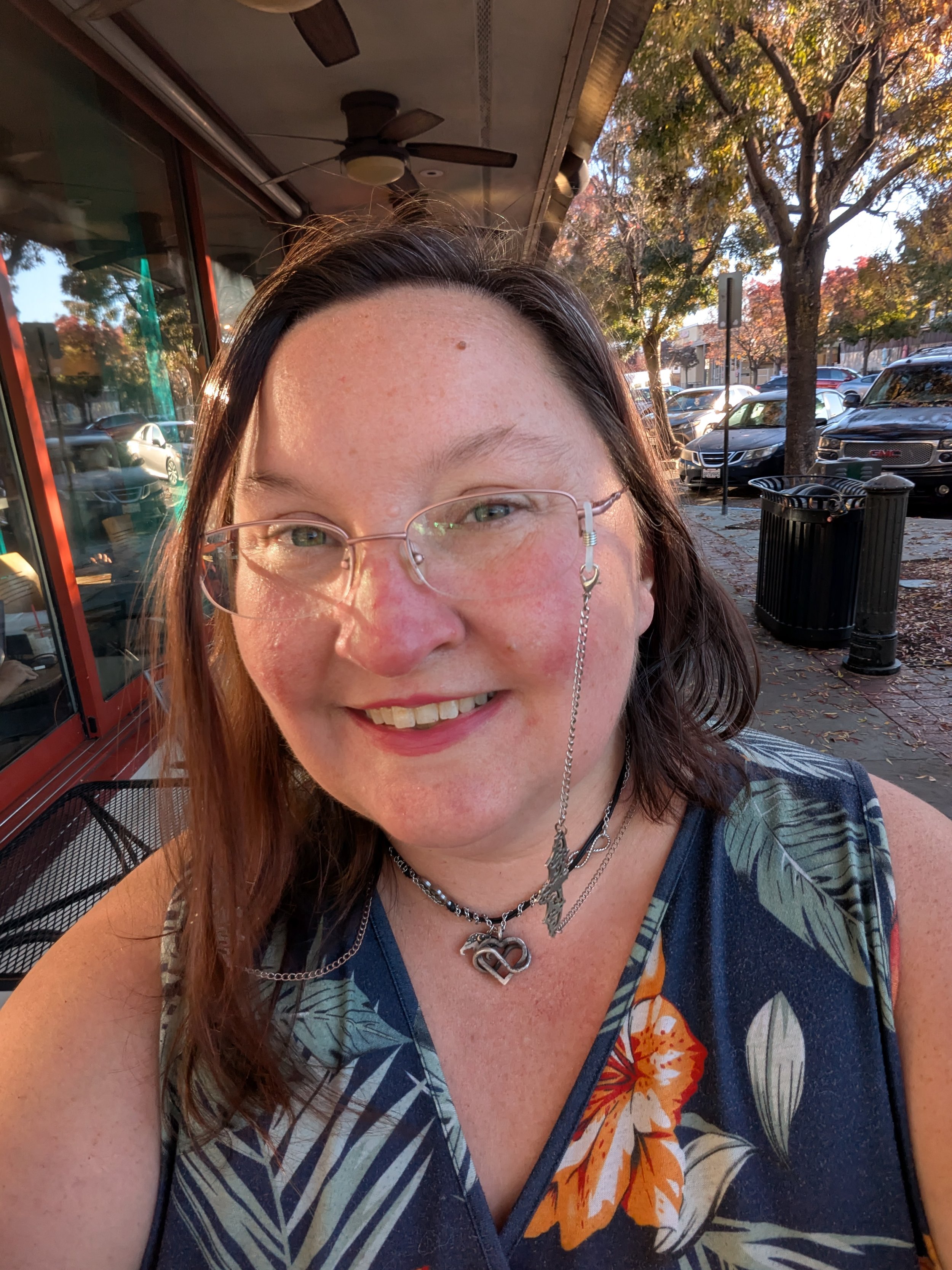 A photo of Wendy, who has medium-length brown hair and glasses. She's sitting outside at a cafe.