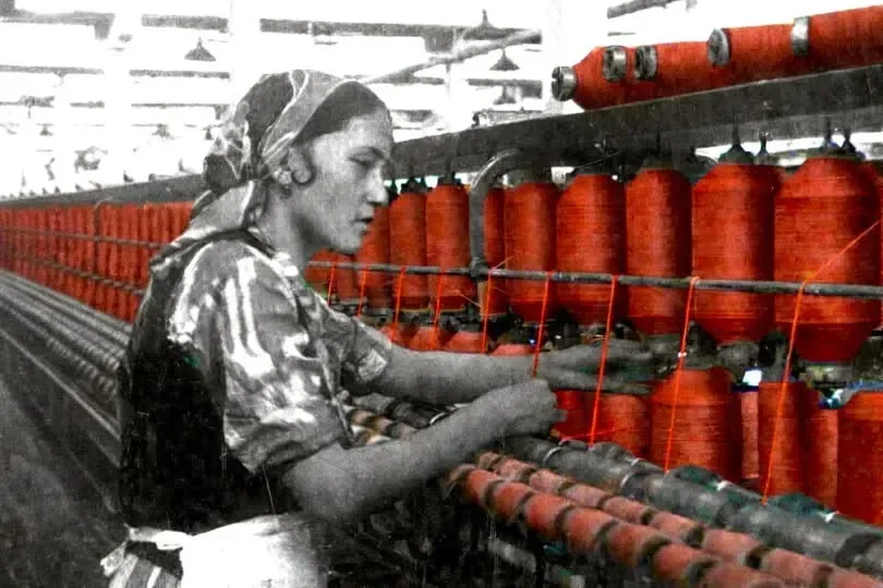 A woman working on red spools of thread in a textile weaving factory.