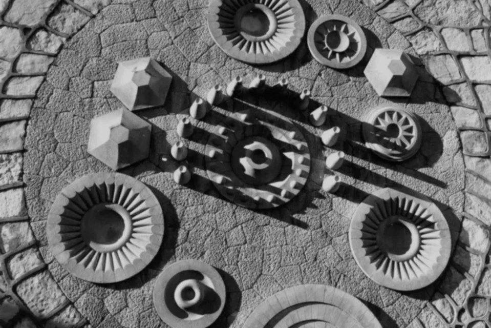 Black and white photo of a wall with various geometric and abstract shapes, including circular, hexagonal, and spiral elements, attached to a textured surface.
