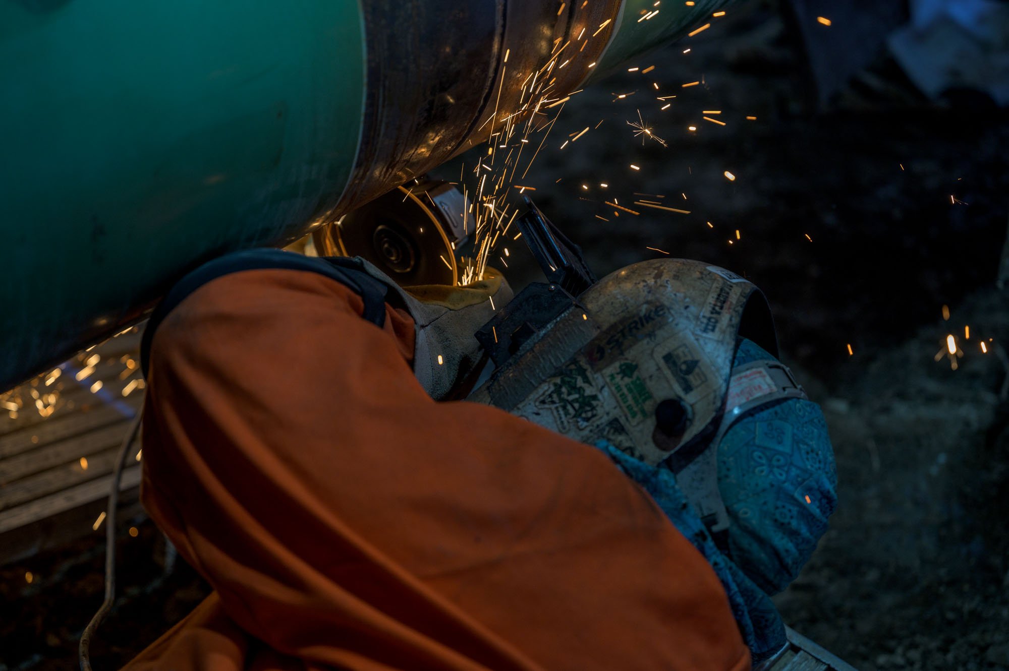 A person welding metal outdoors at night, sparks flying.