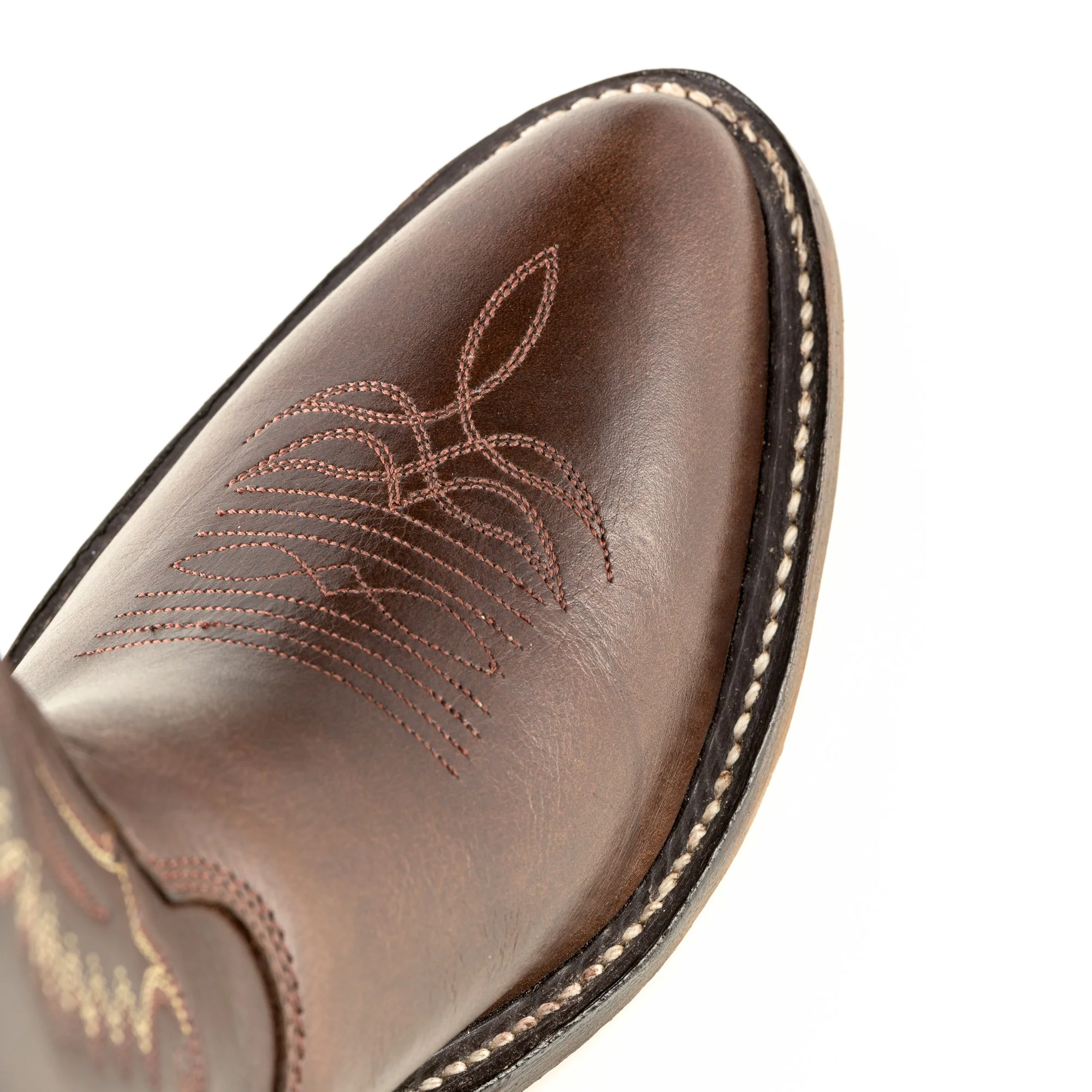 Close-up of a brown leather dress shoe with decorative stitching and white welt stitching around the sole.
