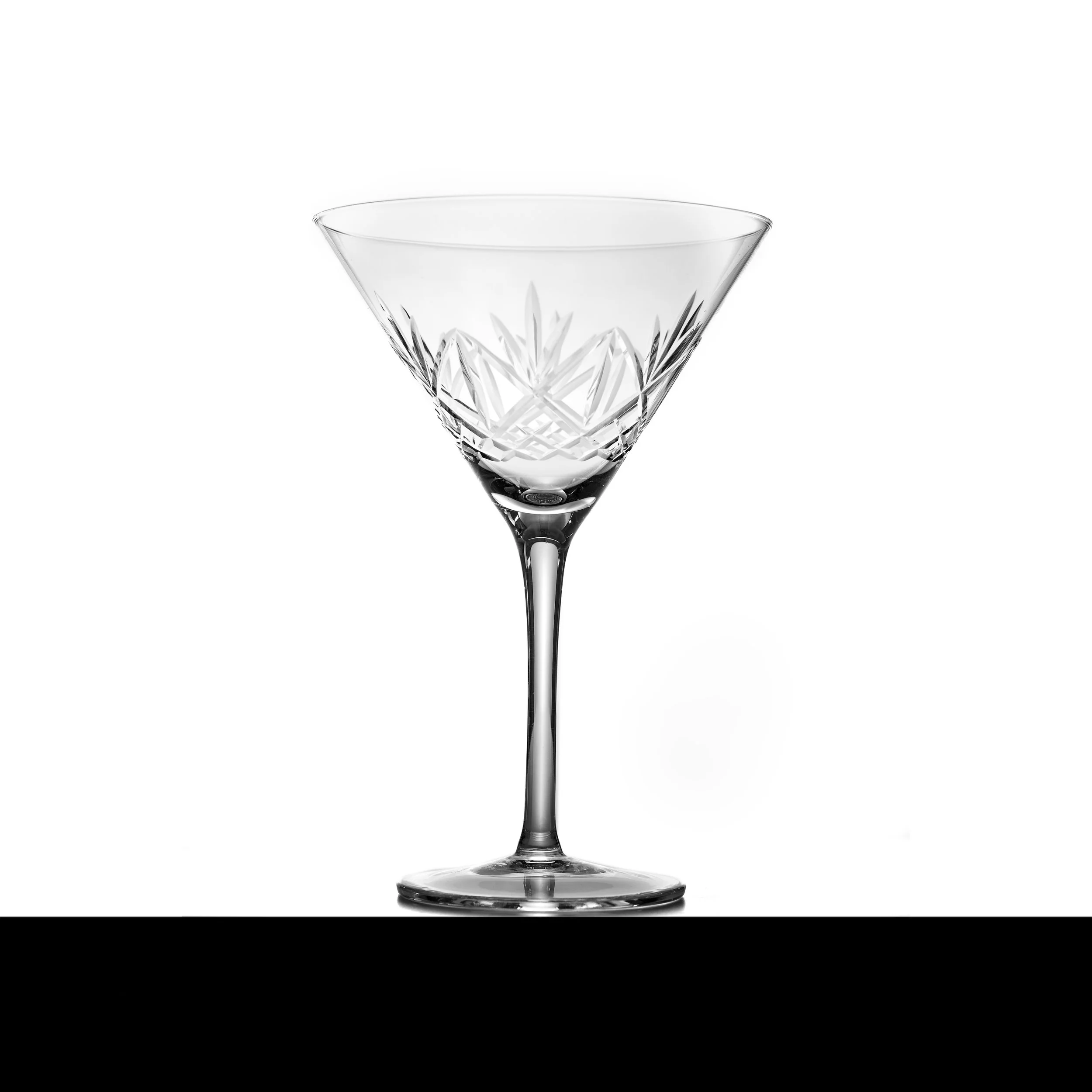 A clear, cut-glass cocktail glass with decorative etching, empty, on a white background.