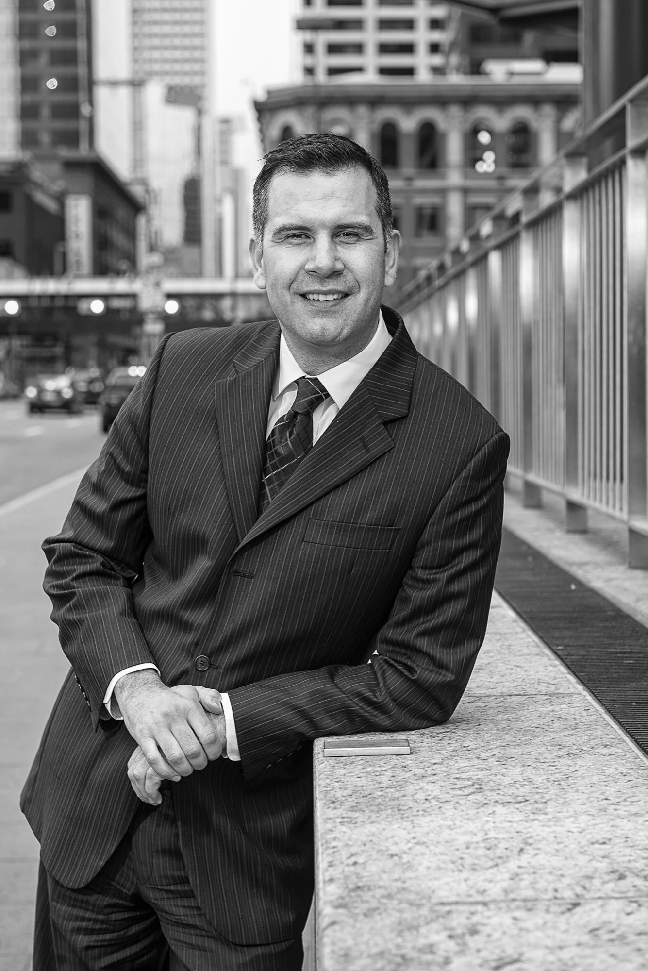 Black and white photo of a man in a business suit leaning on a ledge in an urban area.
