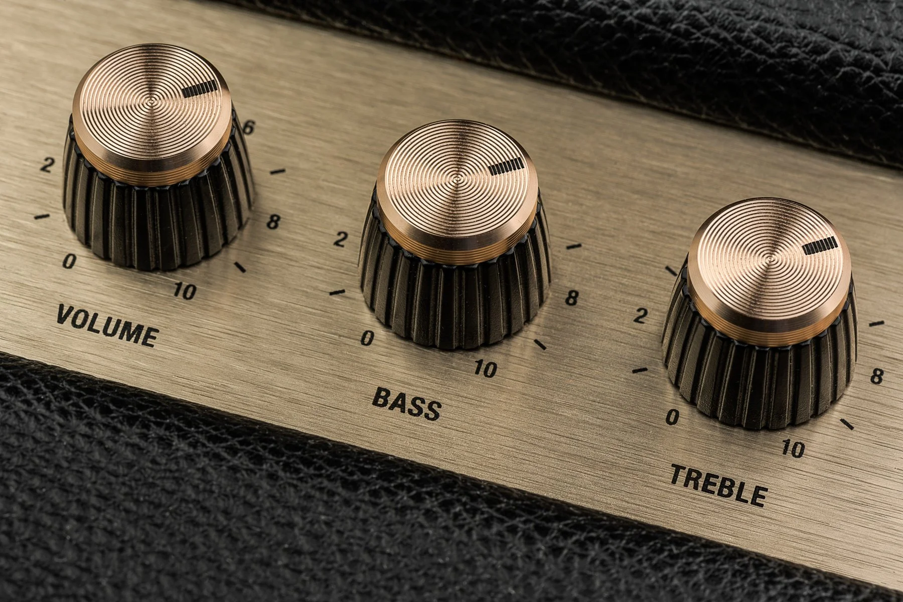 Close-up of a guitar amplifier control panel with three knobs labeled volume, bass, and treble, each with a metallic top and black ridged sides.