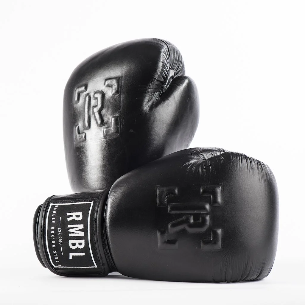 A pair of black boxing gloves, with the brand RMBL visible on the wrist strap, placed against a plain white background.