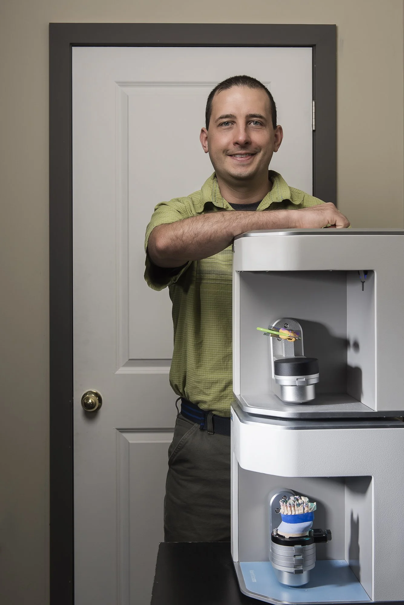 Man standing beside a dental 3D printer in a room.