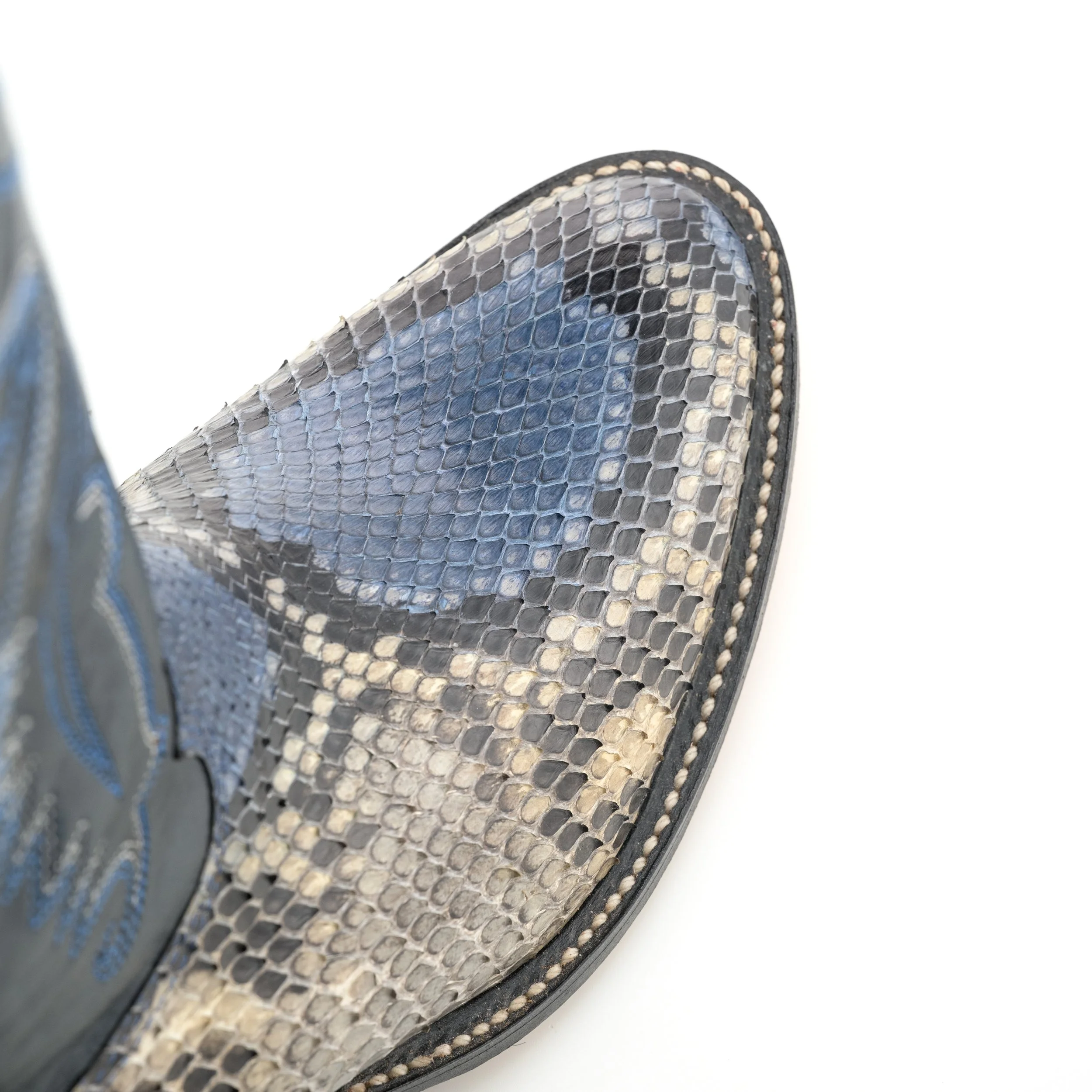Close-up of a pointed toe of a snake skin pattern shoe with detailed stitching along the sole.