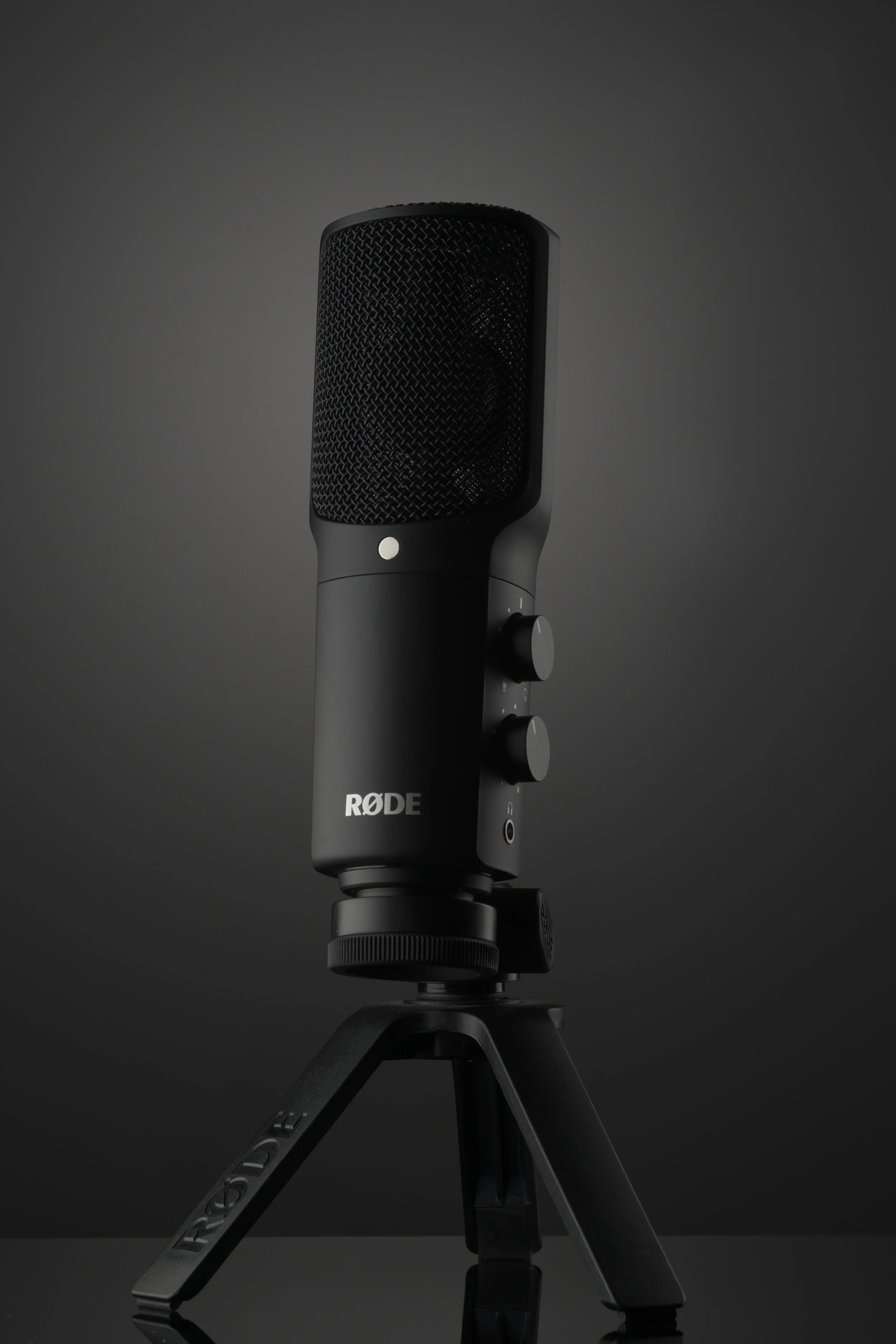 A black RØDE microphone mounted on a small tripod against a dark background.