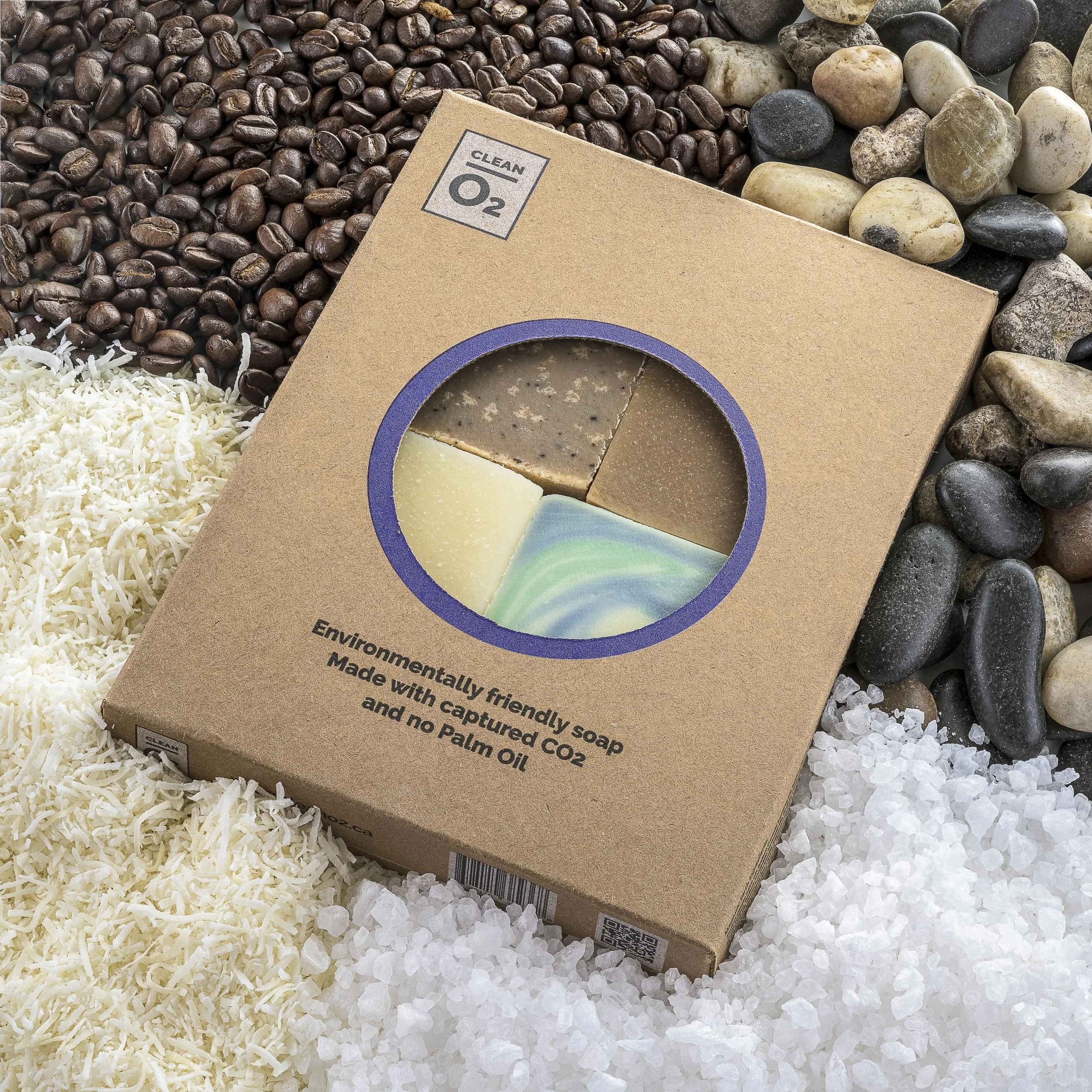 Eco-friendly soap packaging surrounded by coffee beans, shells, salt, and rocks.