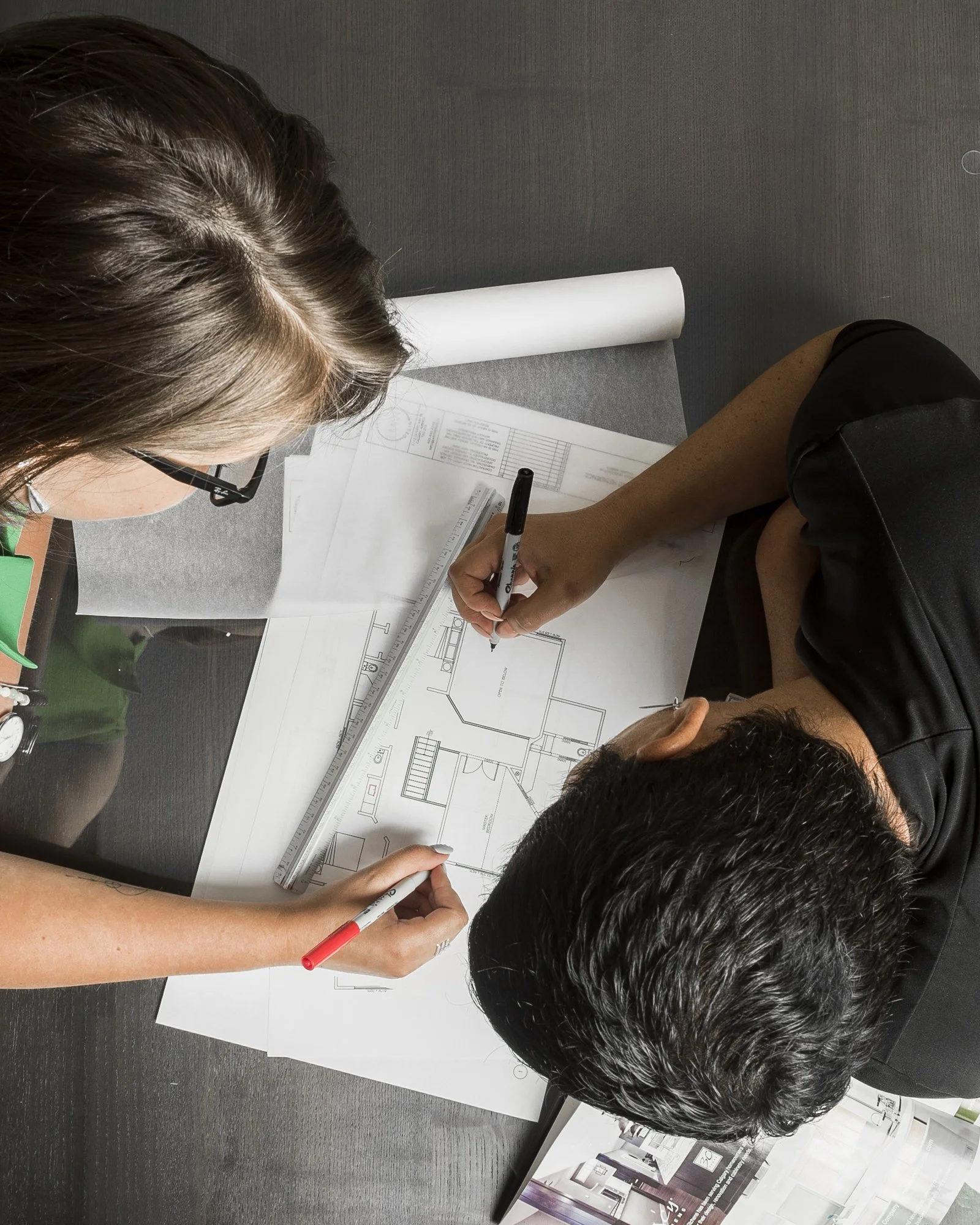 Two people reviewing and marking architectural blueprints on a table.