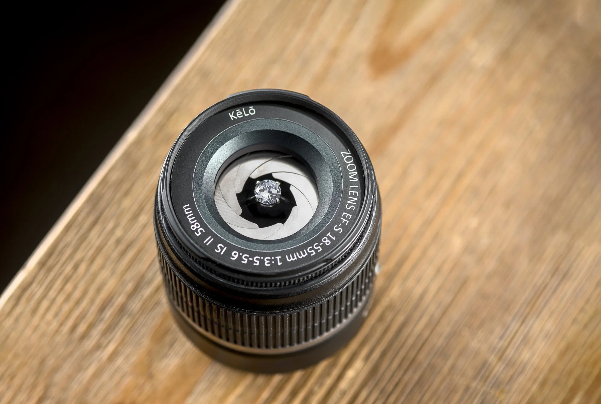 Camera lens with a diamond at the center, placed on a wooden surface, viewed from above.