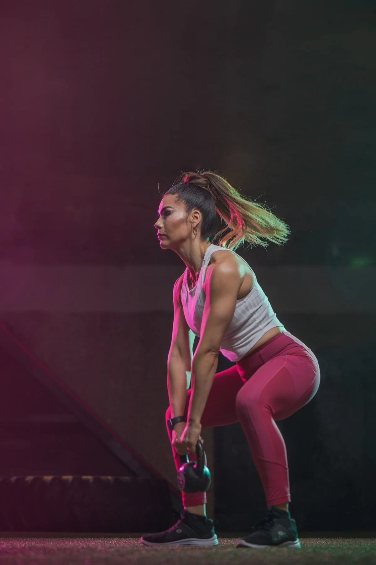 A woman with a colored ponytail doing a bent-over kettlebell exercise in a gym.