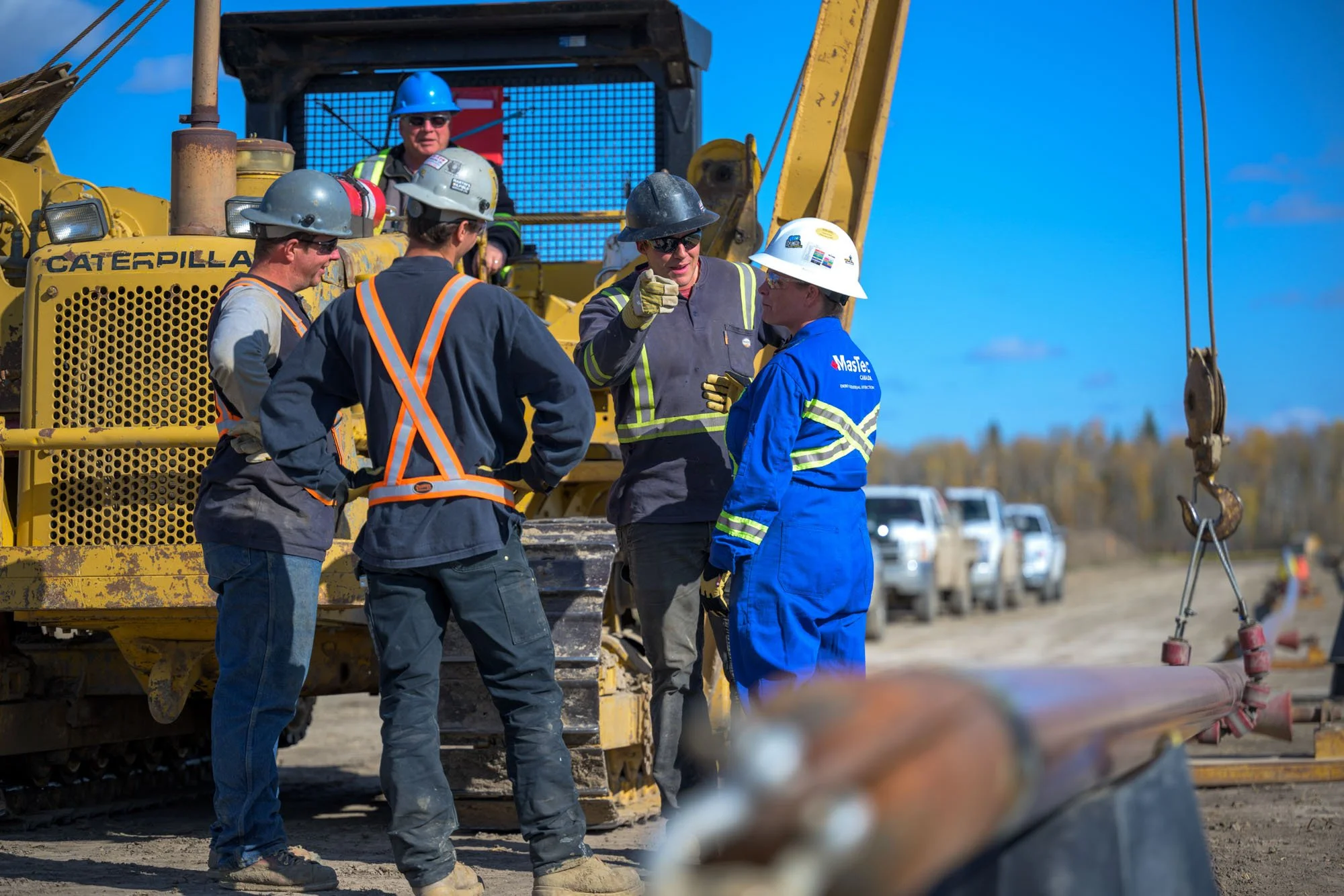 Group of construction workers and engineers having a discussion on a construction site with heavy machinery and pipes.