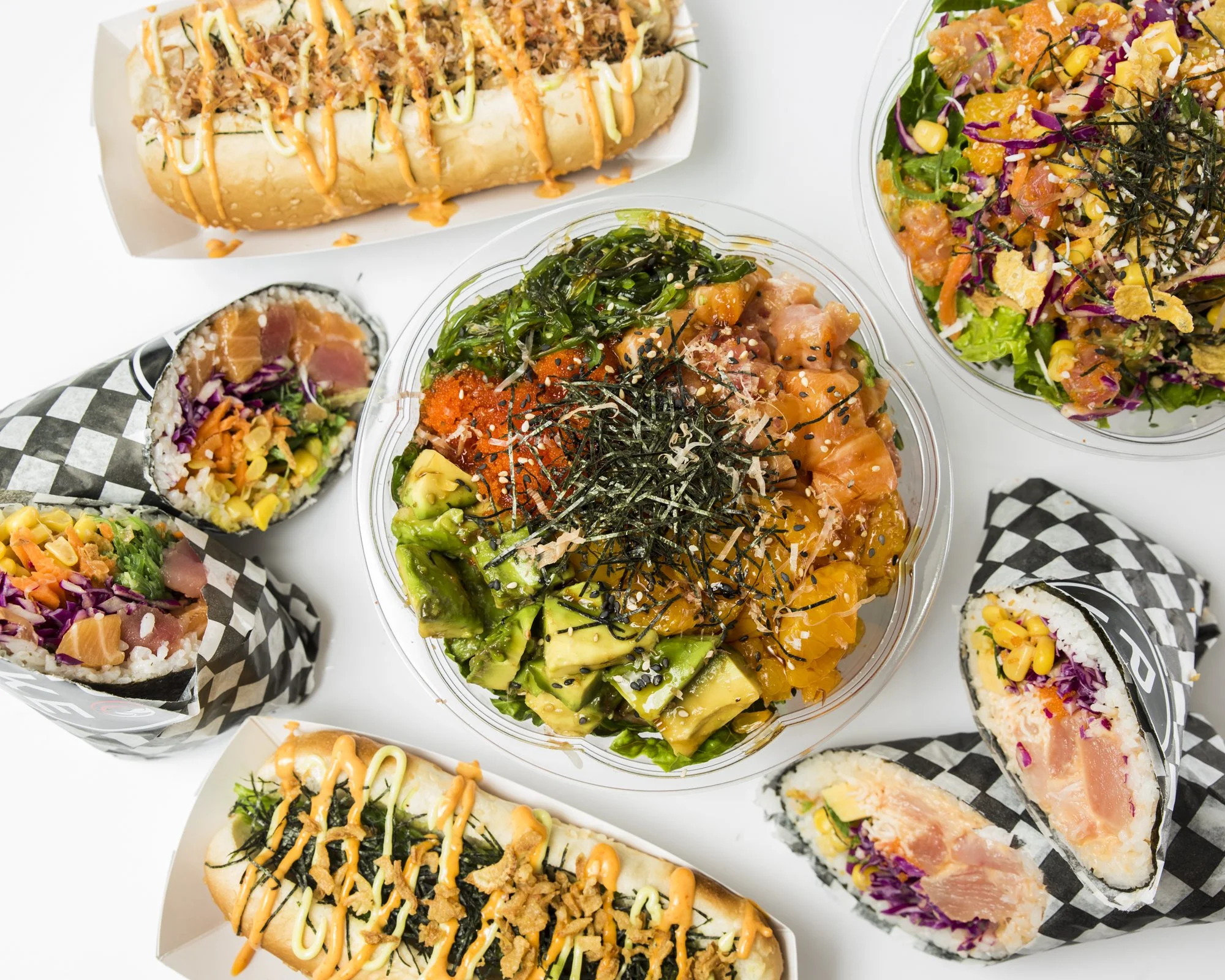 Variety of Asian-style sushi rolls and a salad with seaweed, salmon, avocado, and rice, displayed on a white background.