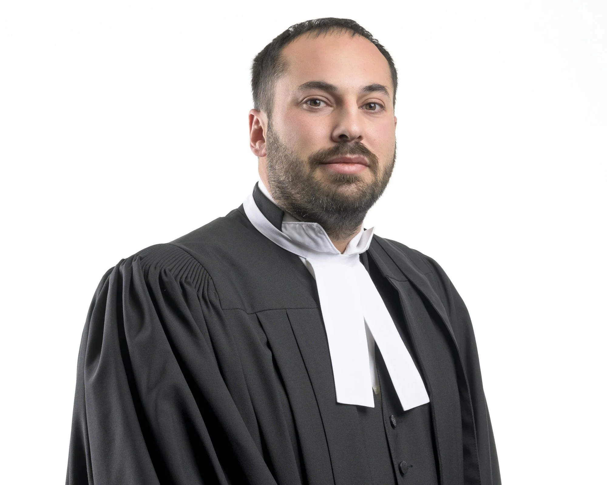 A man dressed in a professional judicial or academic gown with a white neckband, standing against a plain white background.