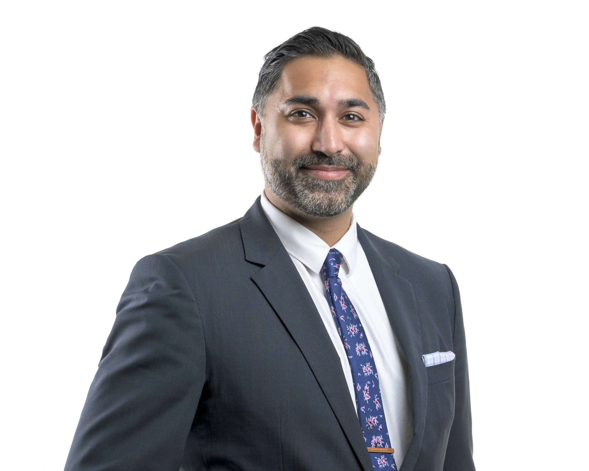 Professional man in a dark suit, white shirt, and patterned tie, smiling against a plain white background.