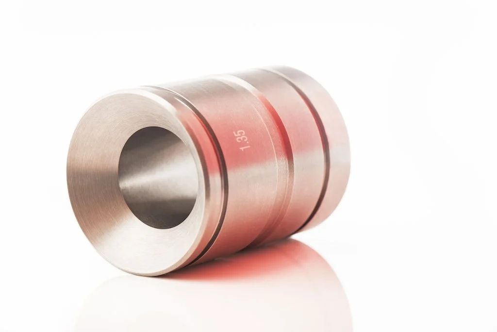 A metal roller with a shiny, metallic surface and engraved numbers, lying on a smooth white surface.