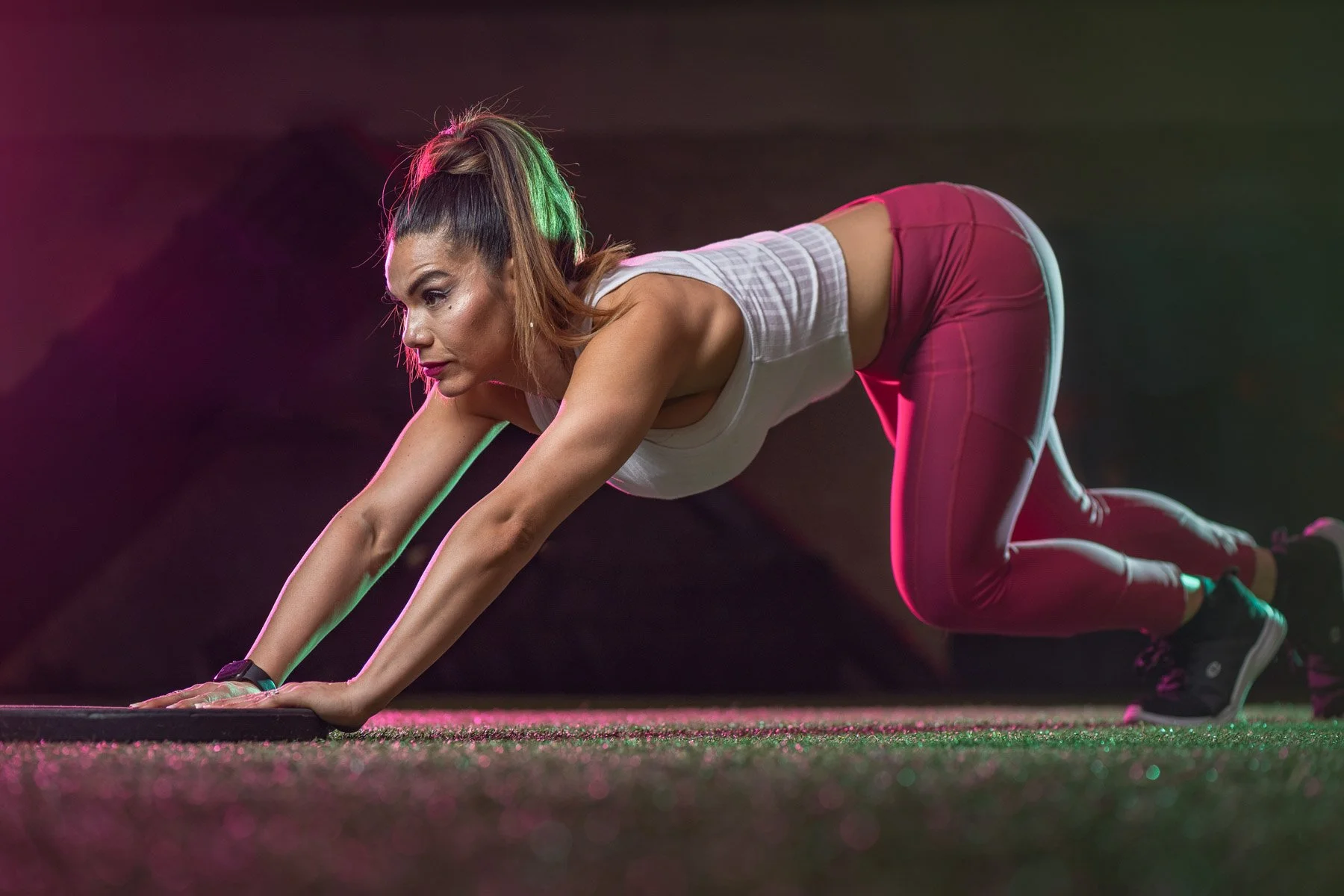 Woman in athletic clothing performing a plank exercise on a gym floor.