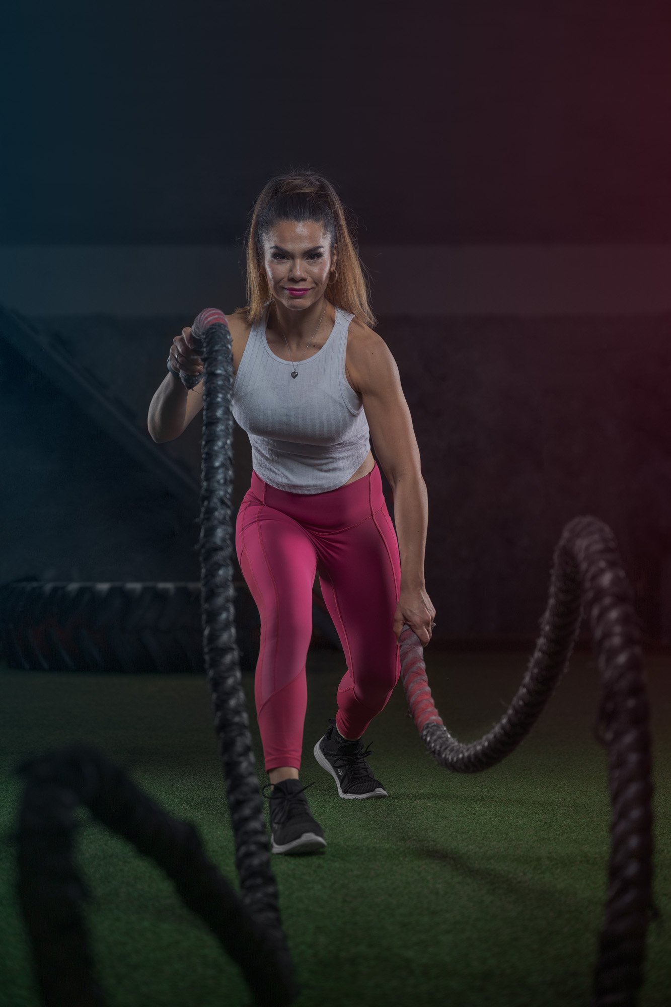 A woman lifting battle ropes in a gym.
