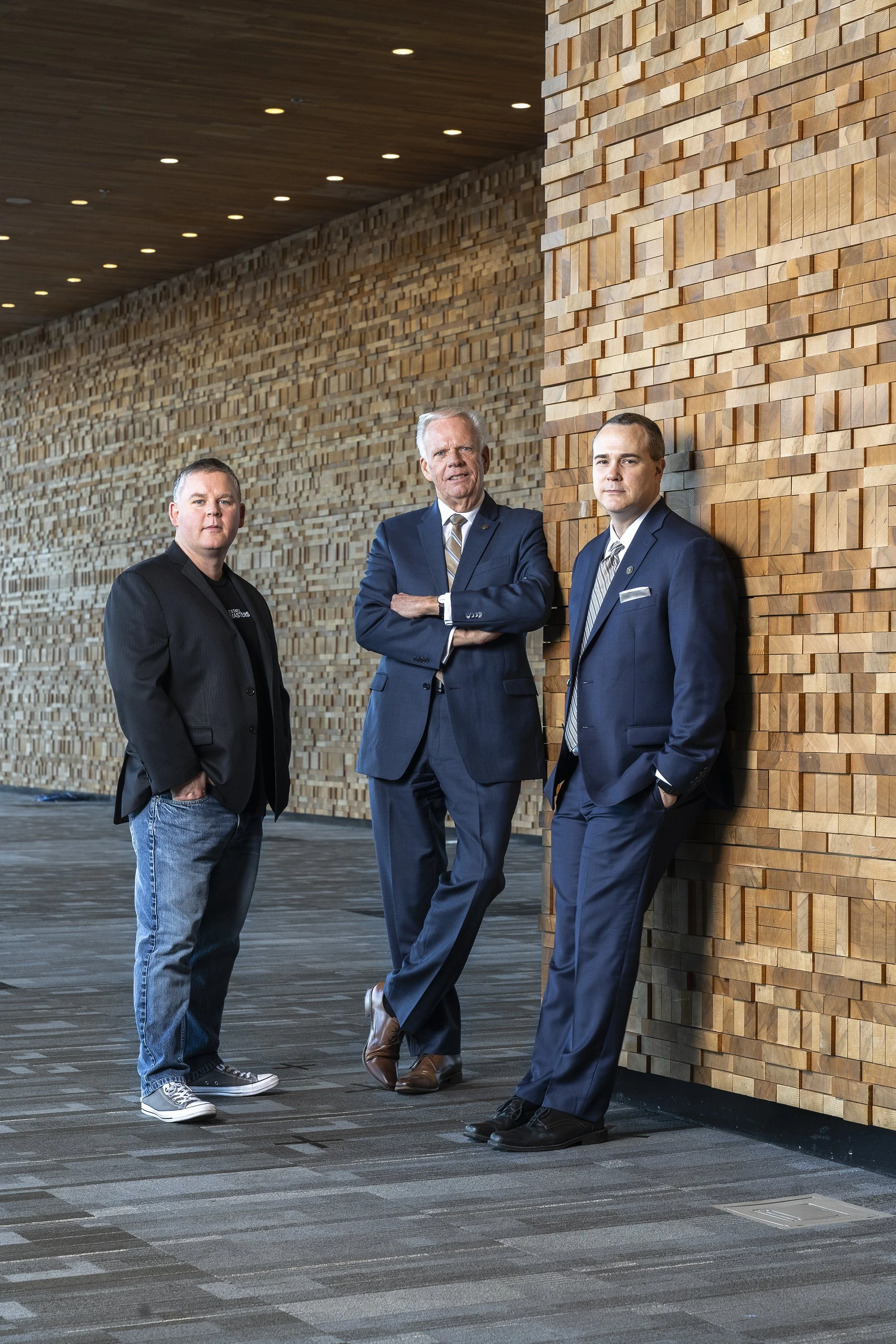 Three men standing against a wooden wall in a modern indoor setting.
