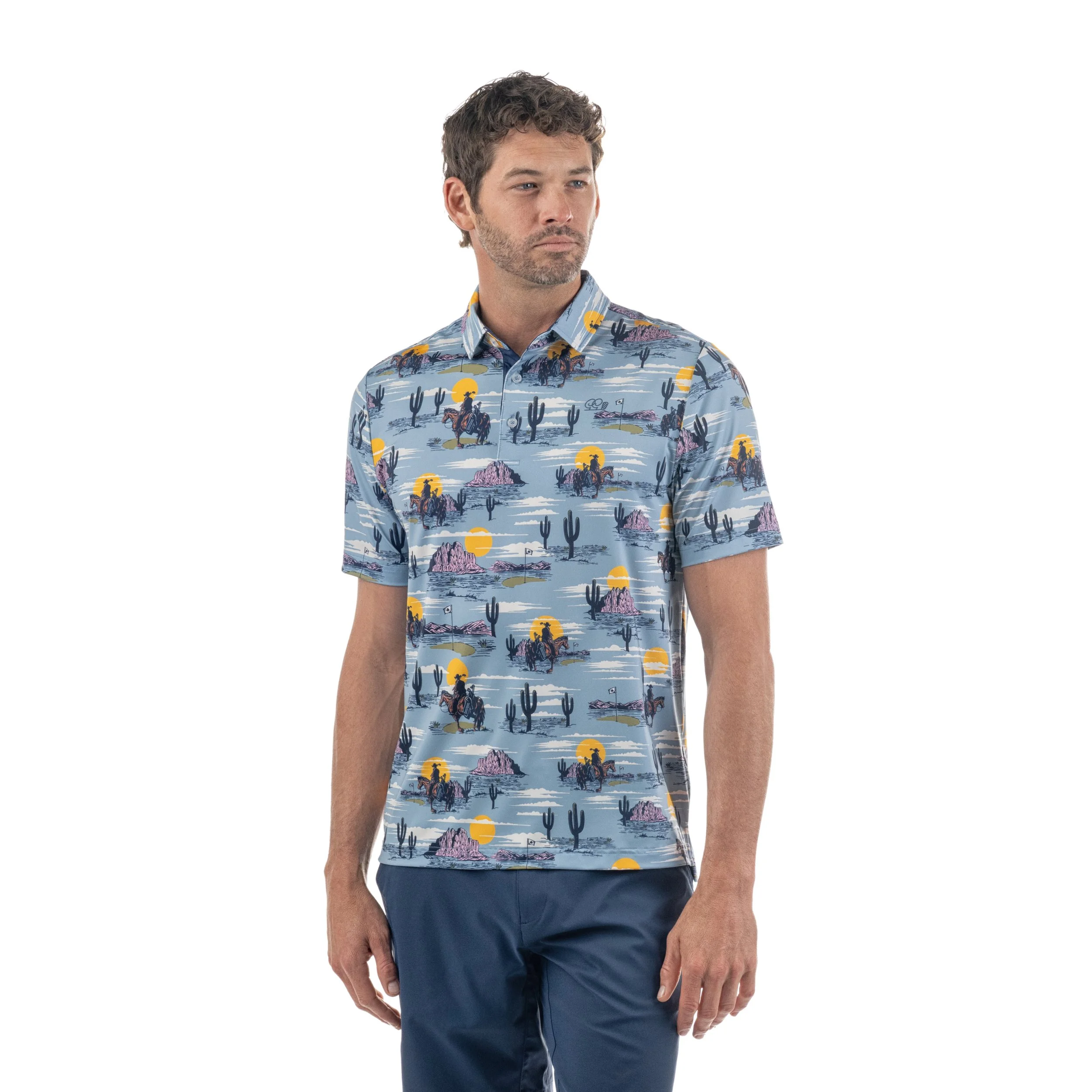 Man wearing a desert-themed short sleeve button-up shirt with cacti, mountains, and sunset illustrations, and navy shorts.