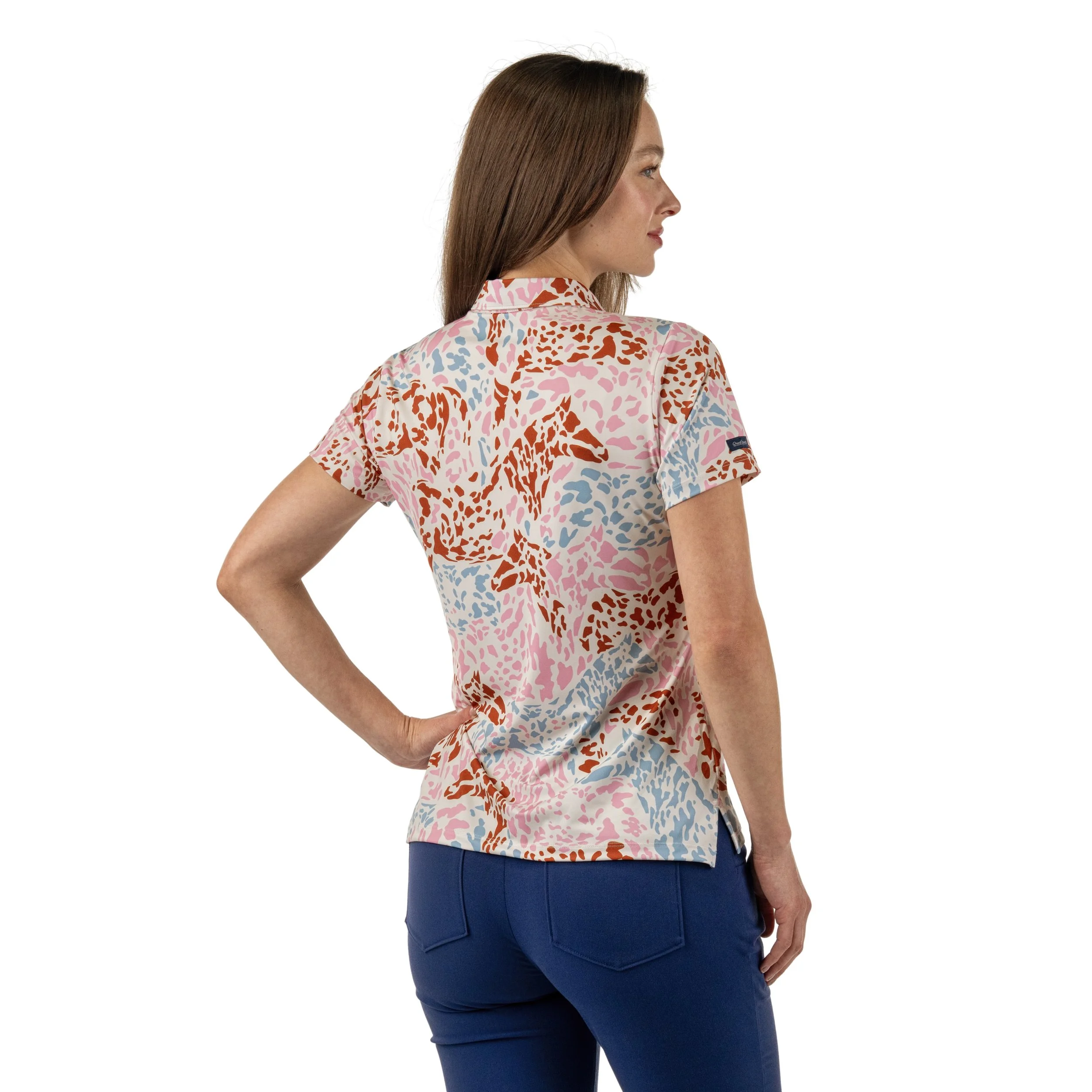 Woman wearing a colorful short-sleeve shirt with a leopard print pattern in pink, blue, brown, and white, paired with blue jeans.