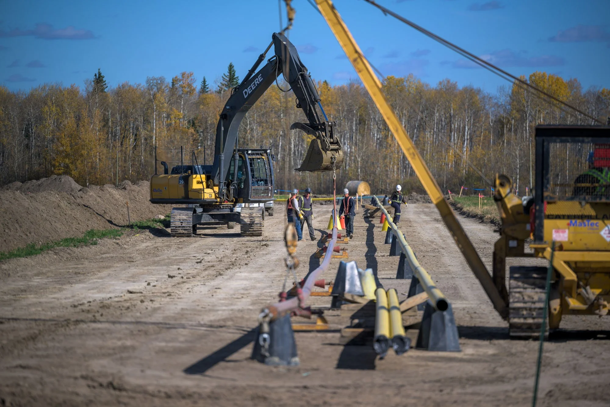 Construction workers and heavy machinery working on a dirt road, with trees in the background.