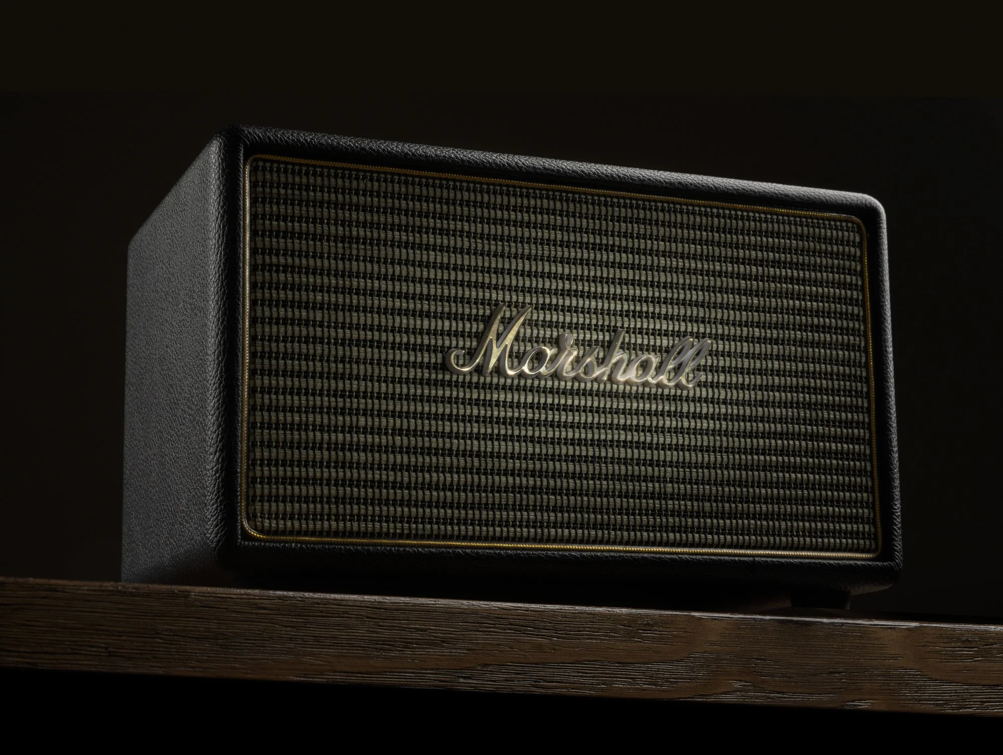 Black Marshall speaker with gold accents placed on a wooden surface with a dark background.