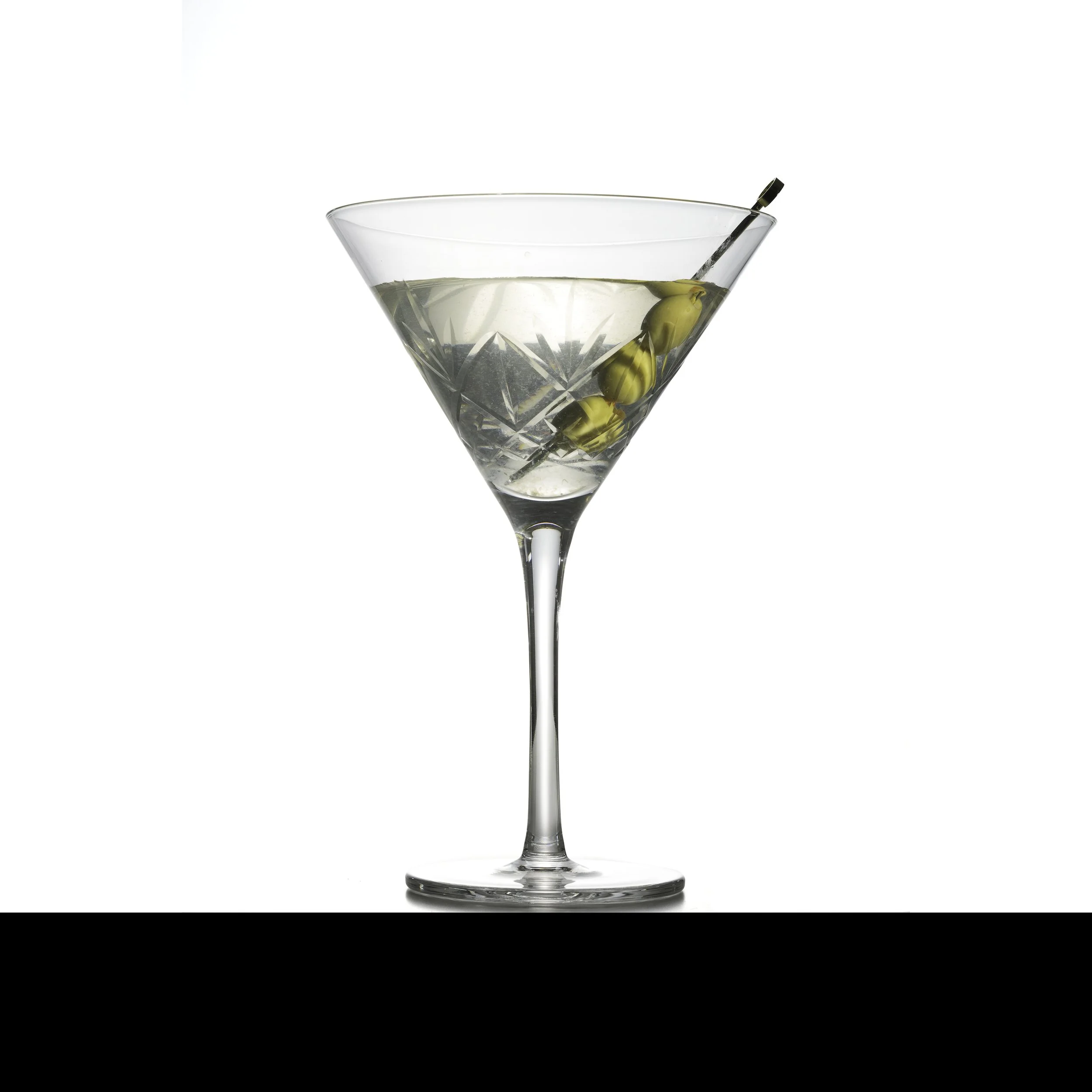 A martini glass filled with a clear cocktail and garnished with green olives on a cocktail pick, against a white background.