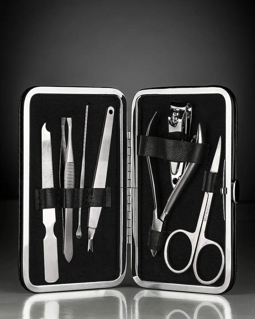 A black case containing stainless steel manicure tools including tweezers, cuticle pusher, nail file, scissors, and a cuticle nipper, organized with elastic straps.