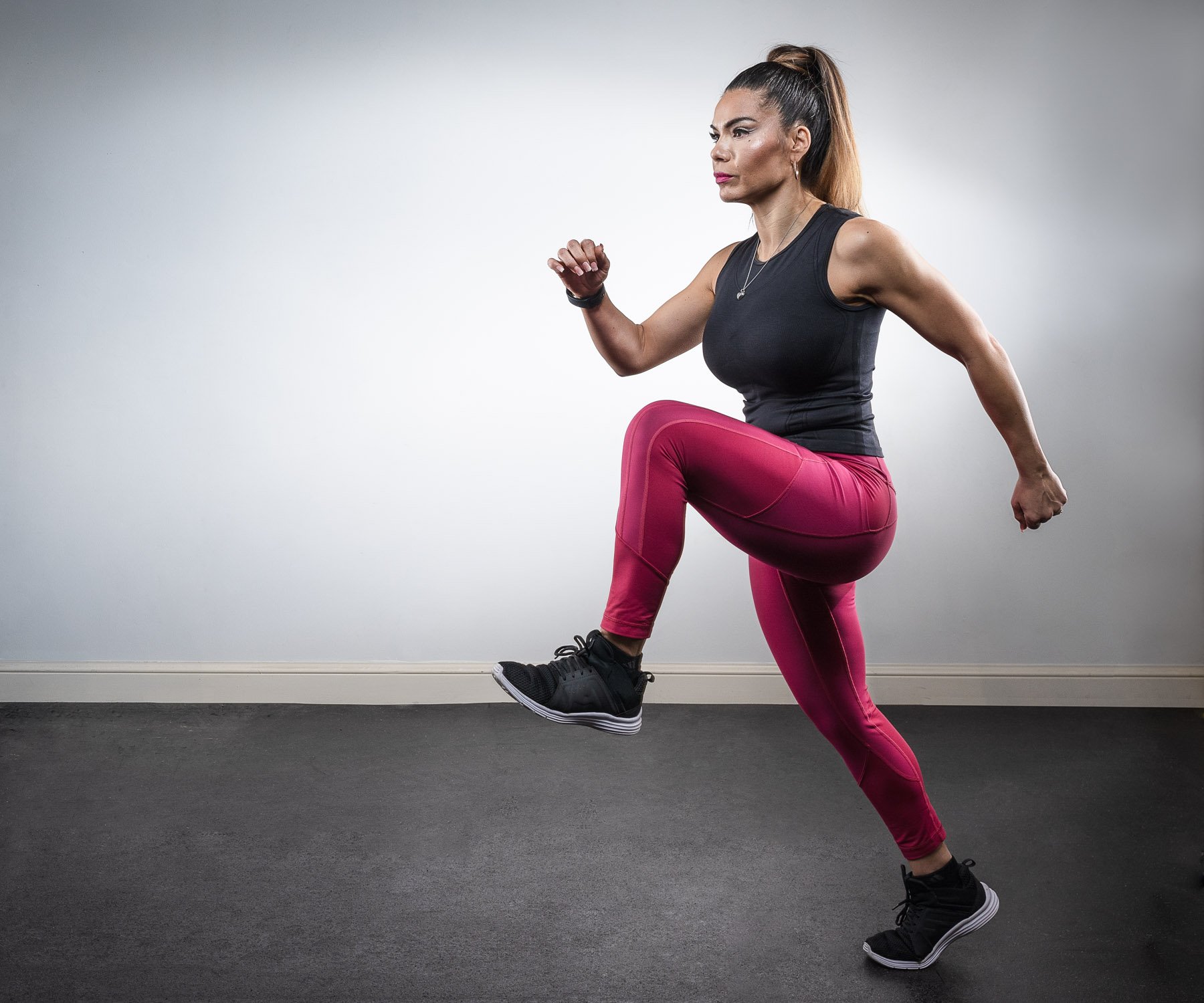 Woman in workout clothes performing a high knee exercise indoors.